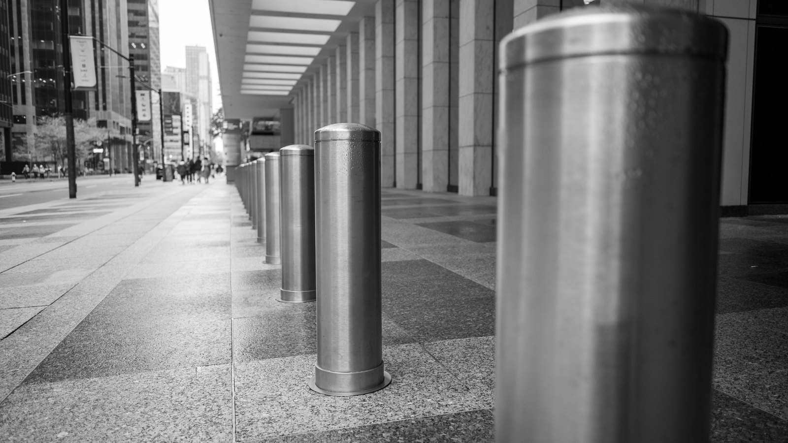 A row of steel security bollards along a city sidewalk.