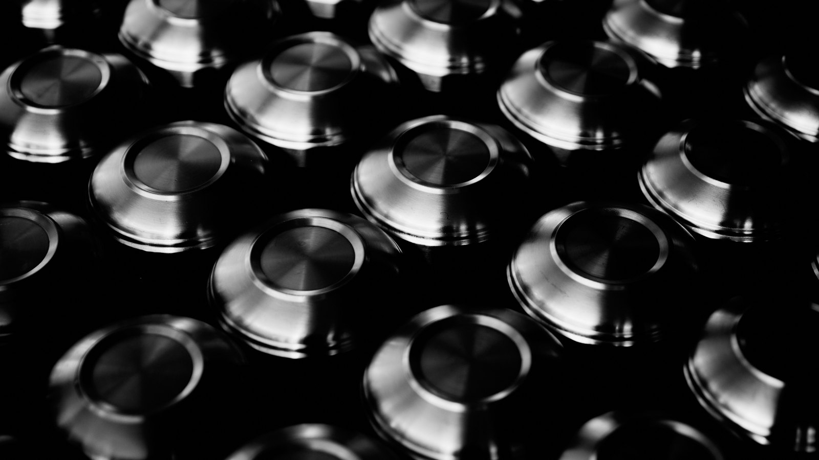 Rows of identical machined circular metal parts packed close together and photographed in black and white under a raking light, each with a turned face and a raised rim catching a bright highlight. No lettering, no markings and no people are in the frame. An illustrative photograph, not connected to this proceeding.