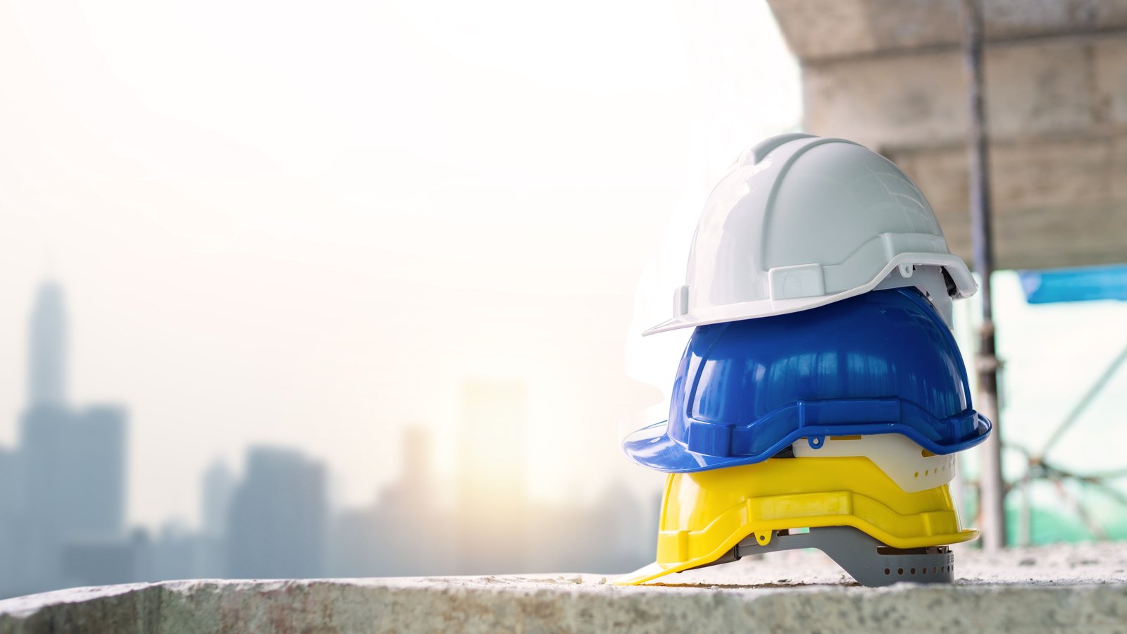 White, blue and yellow safety helmets are stacked at a construction site.