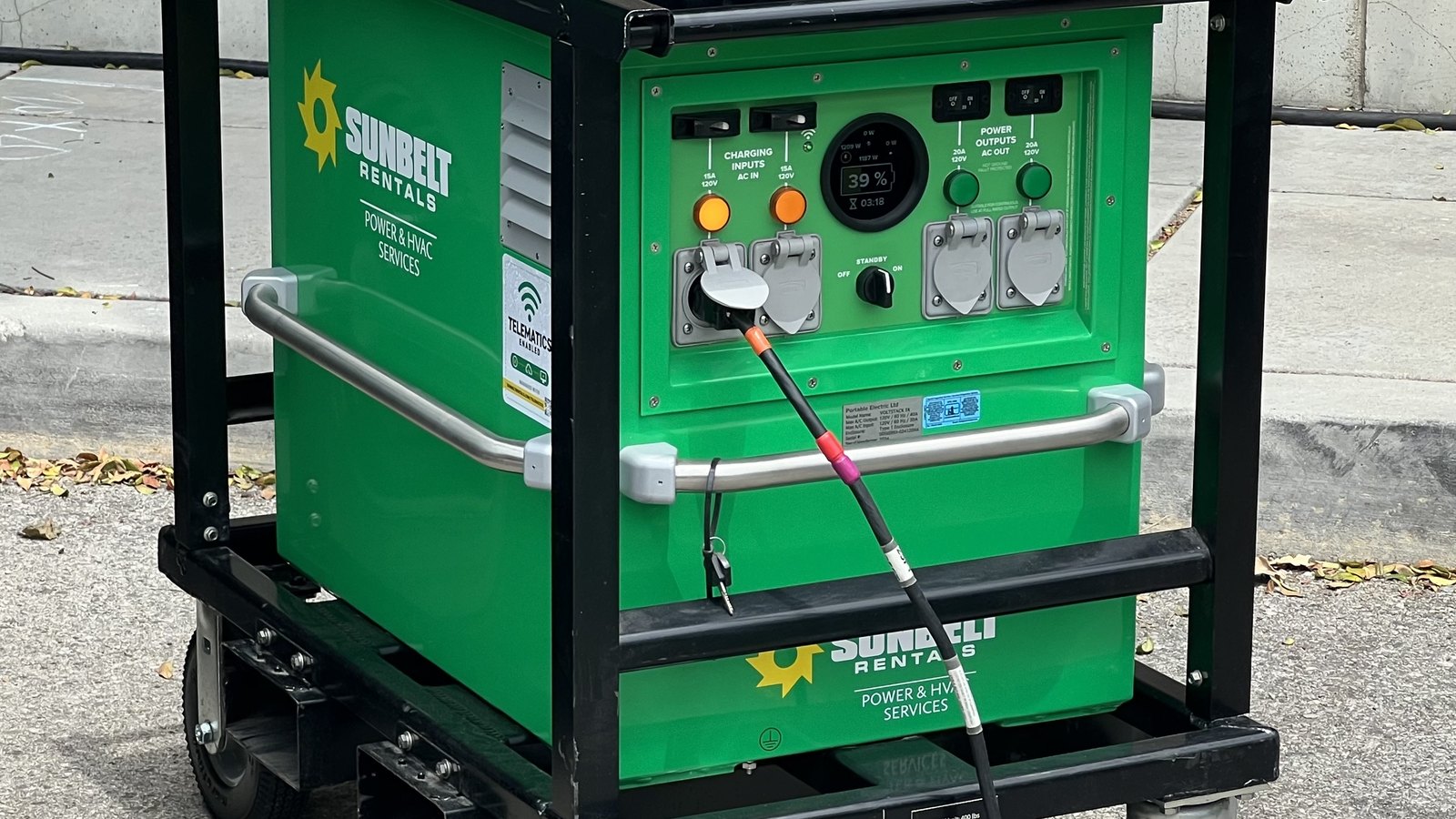 A green Sunbelt Rentals mobile power unit with covered outlets and control switches inside a black steel frame.
