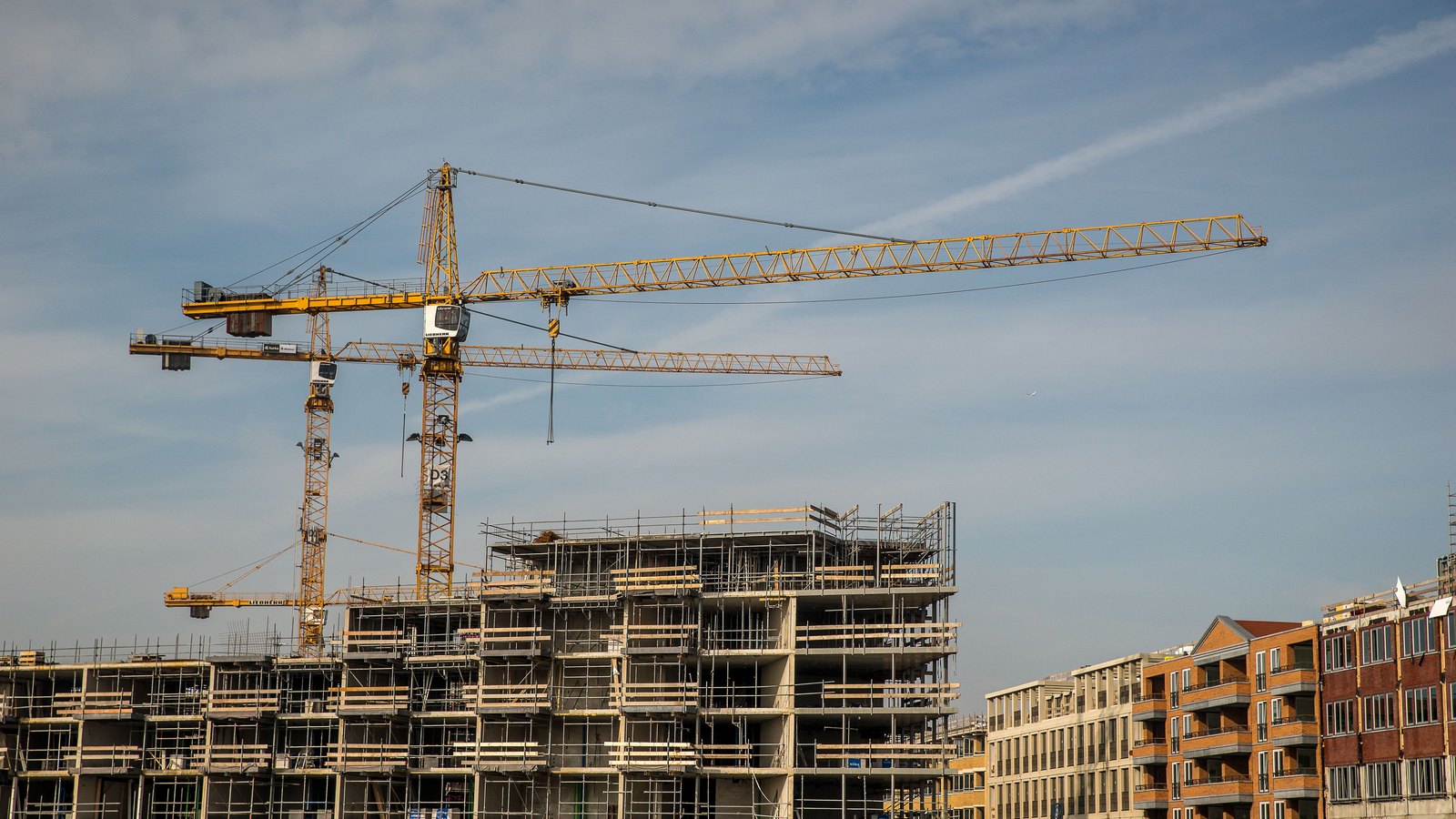 A commercial building under construction with two tower cranes against a blue sky.
