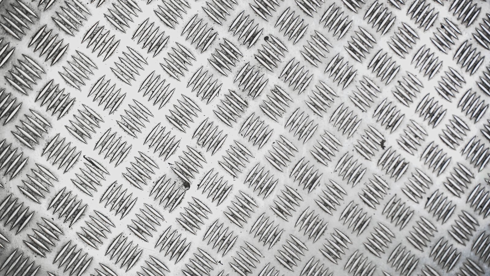A bright steel chequer plate photographed straight on, the raised diamond tread repeating across the whole frame.