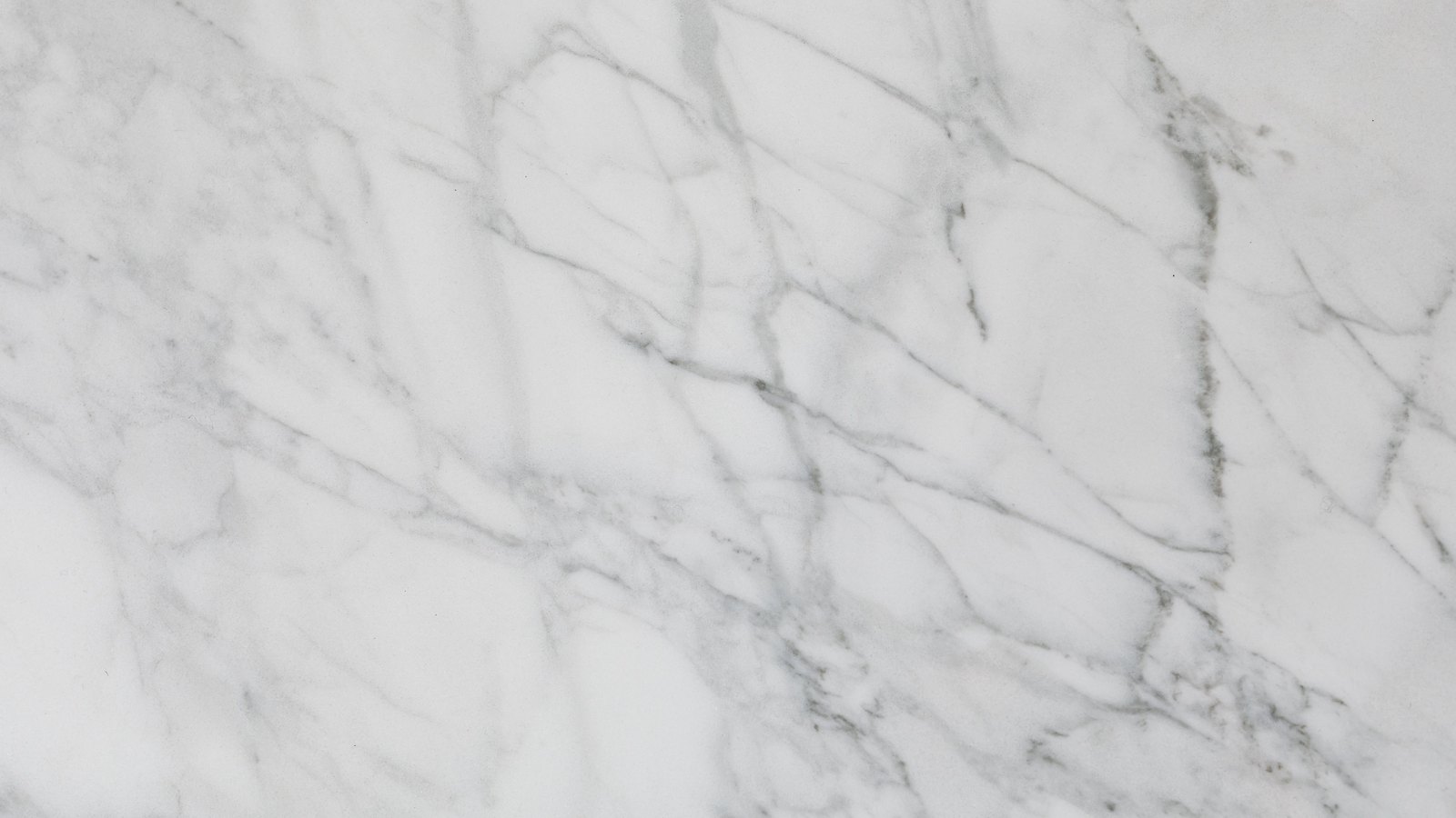 White marble photographed square on and filling the frame. Fine grey veins branch diagonally across the surface, coarser and darker towards the right, thinning to hairlines at the top left. There is no edge, object, lettering or shadow in the picture.