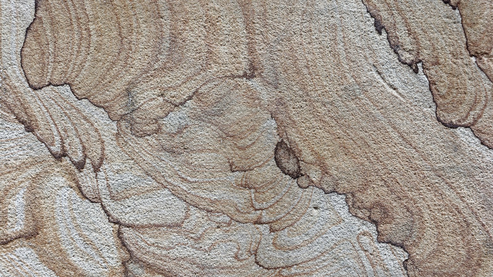 A close photograph of a weathered sandstone face filling the frame, pale grey and buff bands curving across the grainy surface in concentric contour lines with a few darker mineral stains. No object, person, tool, marking or lettering is in view.
