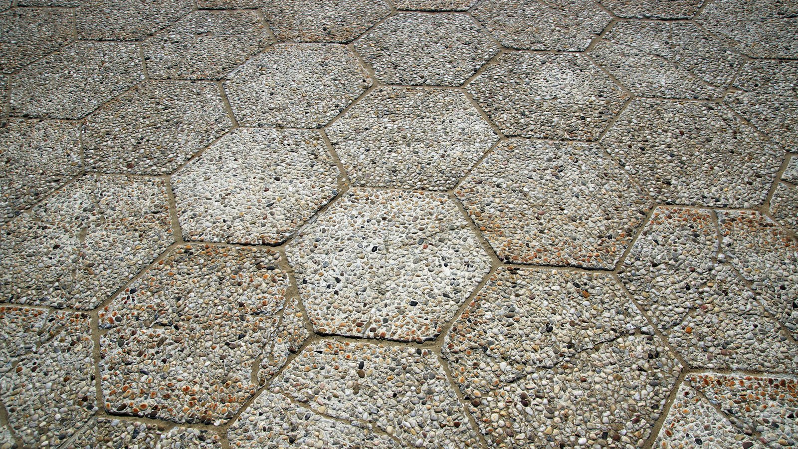 A close overhead photograph of a paved surface filling the whole frame, laid in interlocking hexagonal slabs whose exposed faces are packed with small pale grey and brown pebbles, with narrow joints between them. No text, brand mark, person or identifiable place is in view.