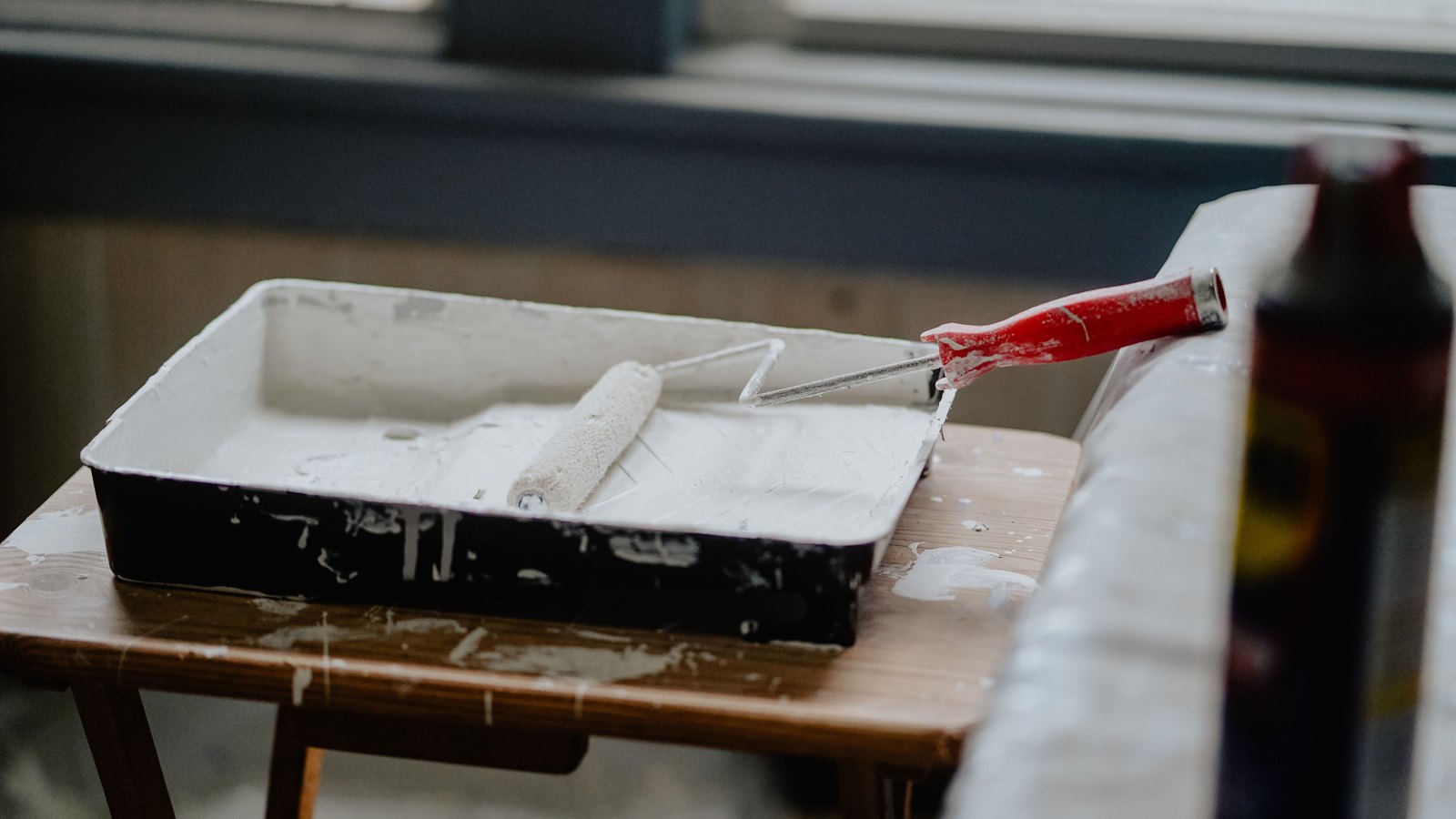 A paint roller rests in a tray of white paint on a wooden table, not a photograph of this trade case.