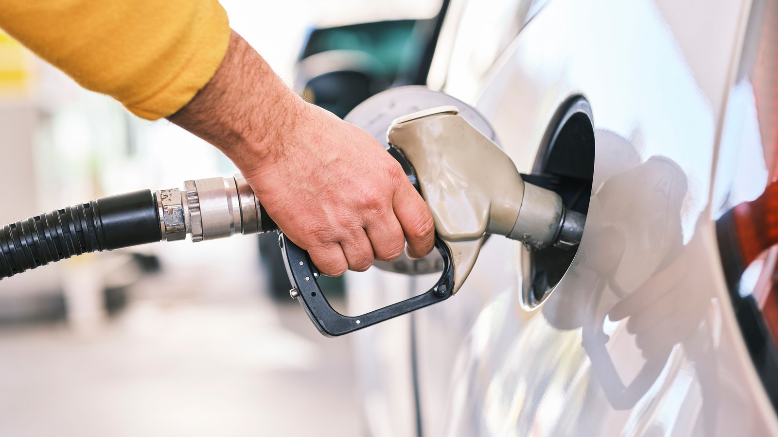 A hand holds an unbranded fuel nozzle in a car's fuel port.