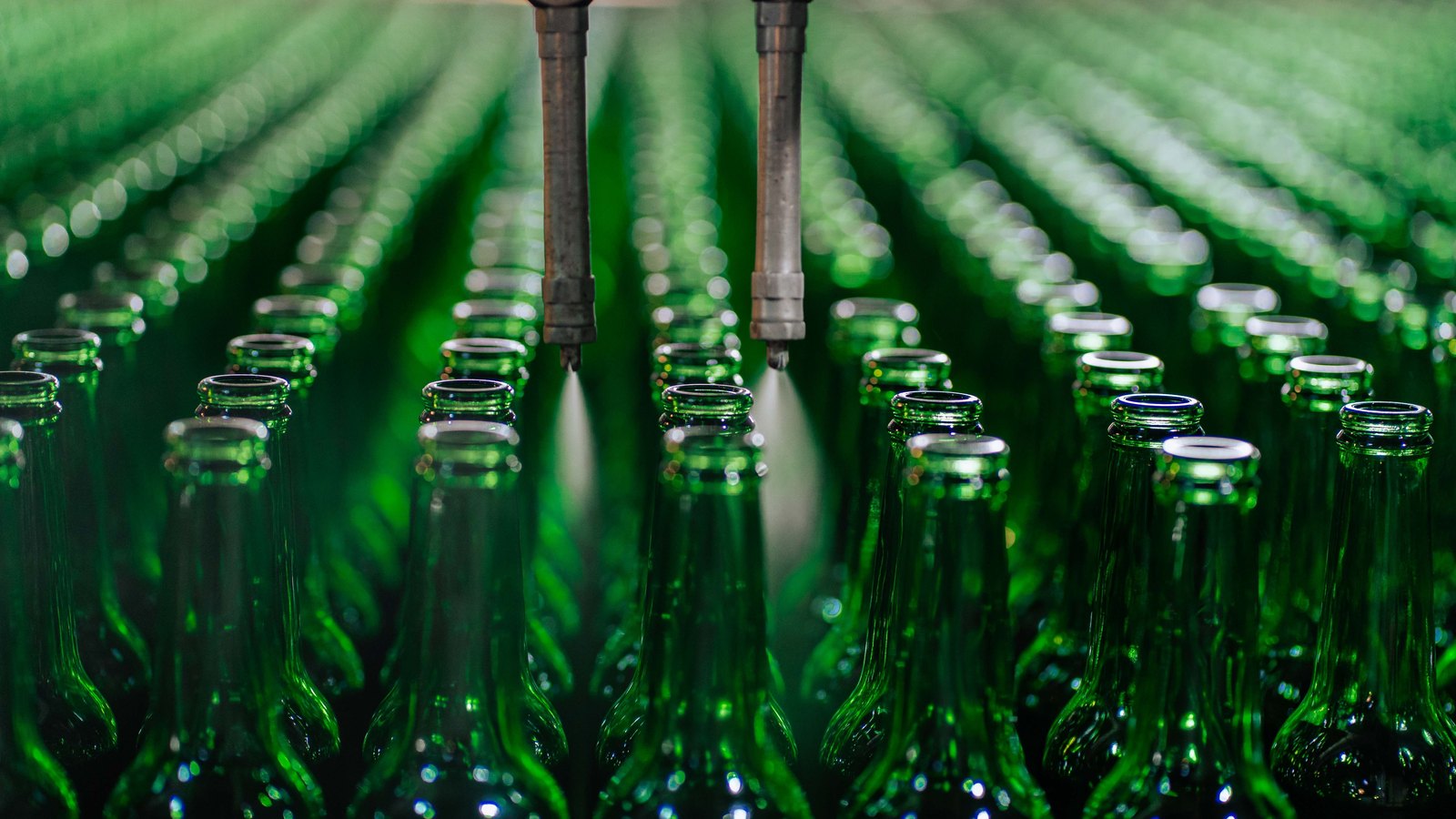 Rows of green glass bottles move through an automated filling line.