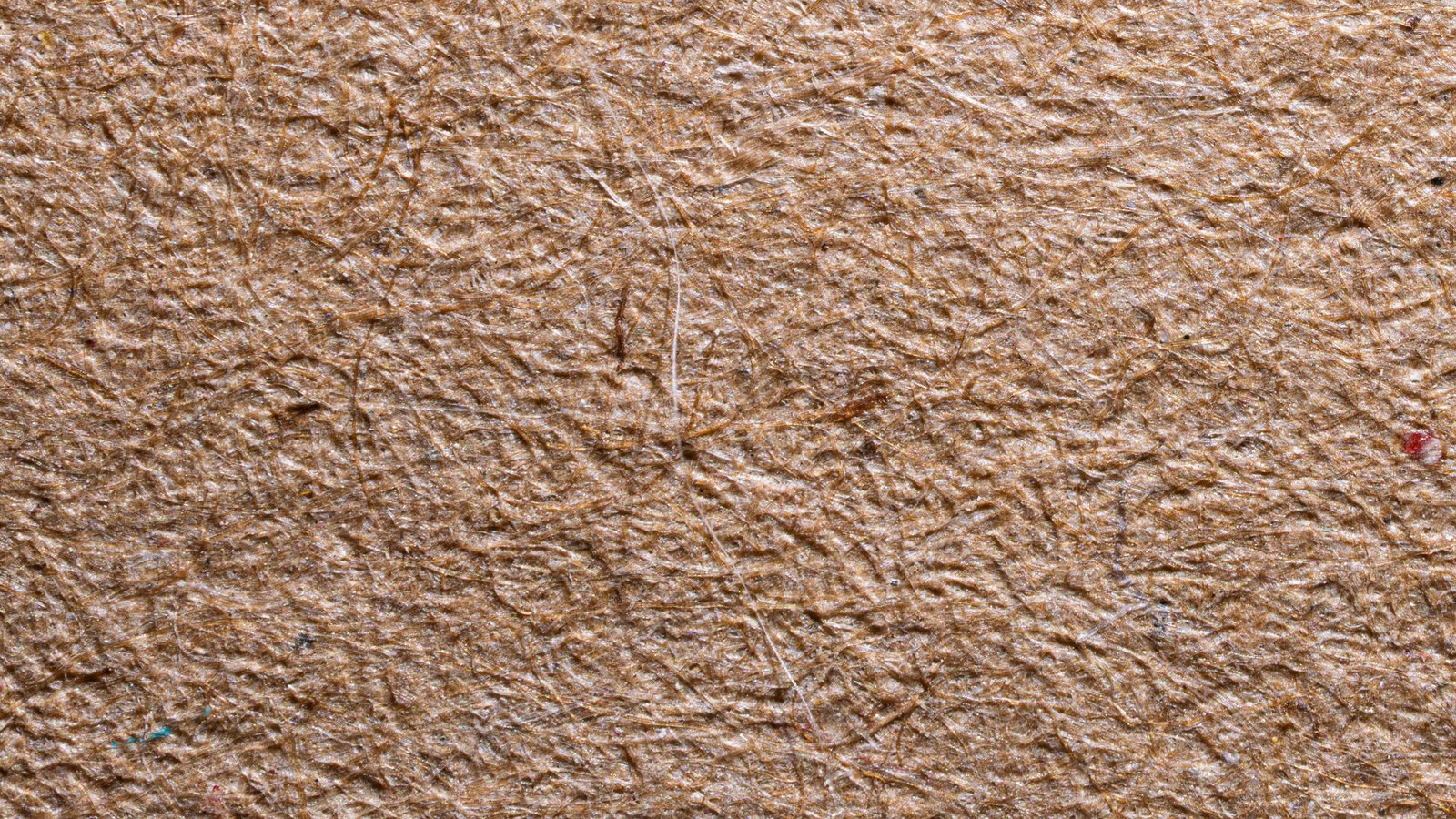 A close view of recycled brown kraft paper, its coarse surface showing pressed fibres and flecks of colour.