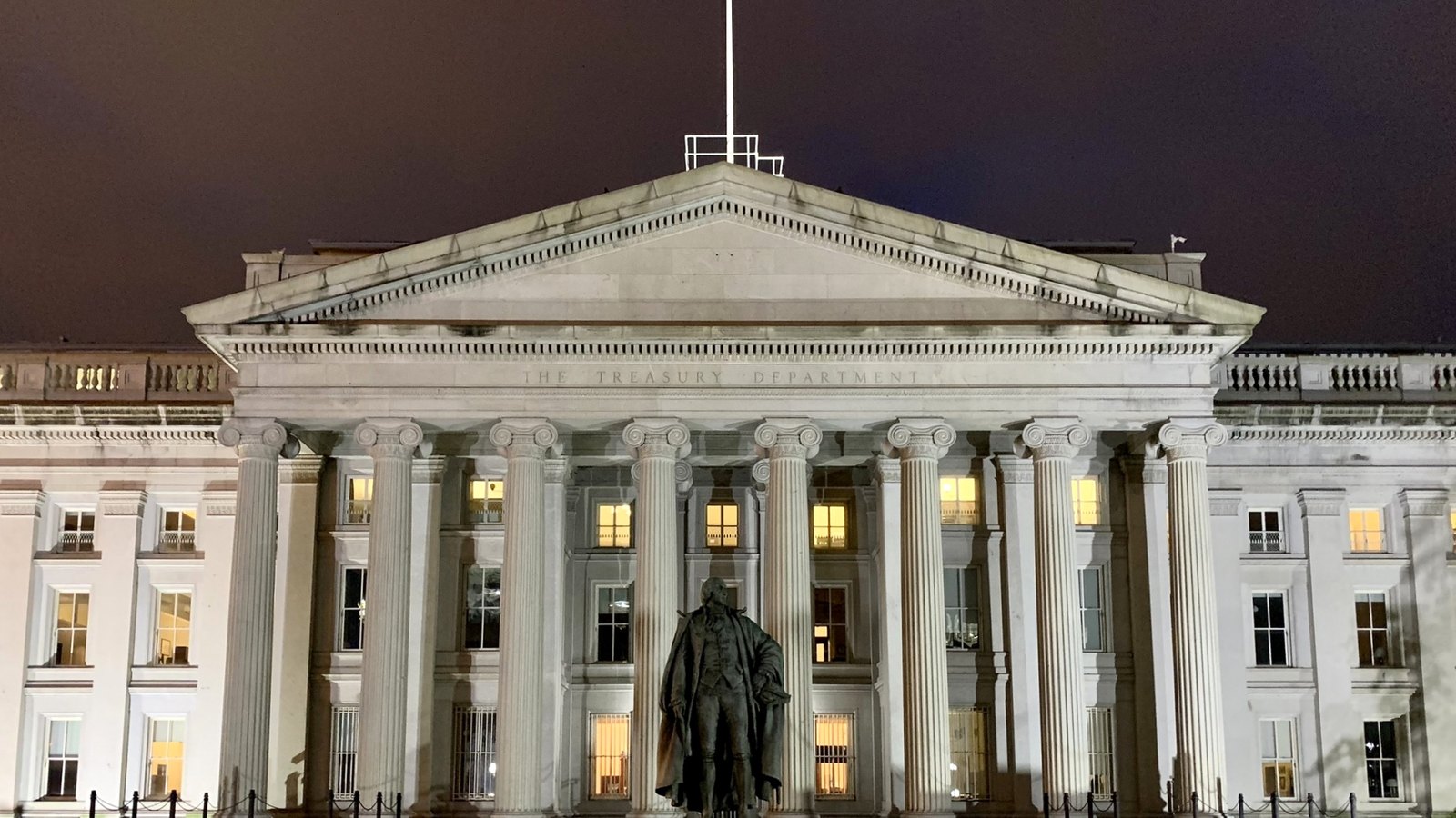 The United States Treasury Building illuminated at night in Washington, centered on its columned portico.