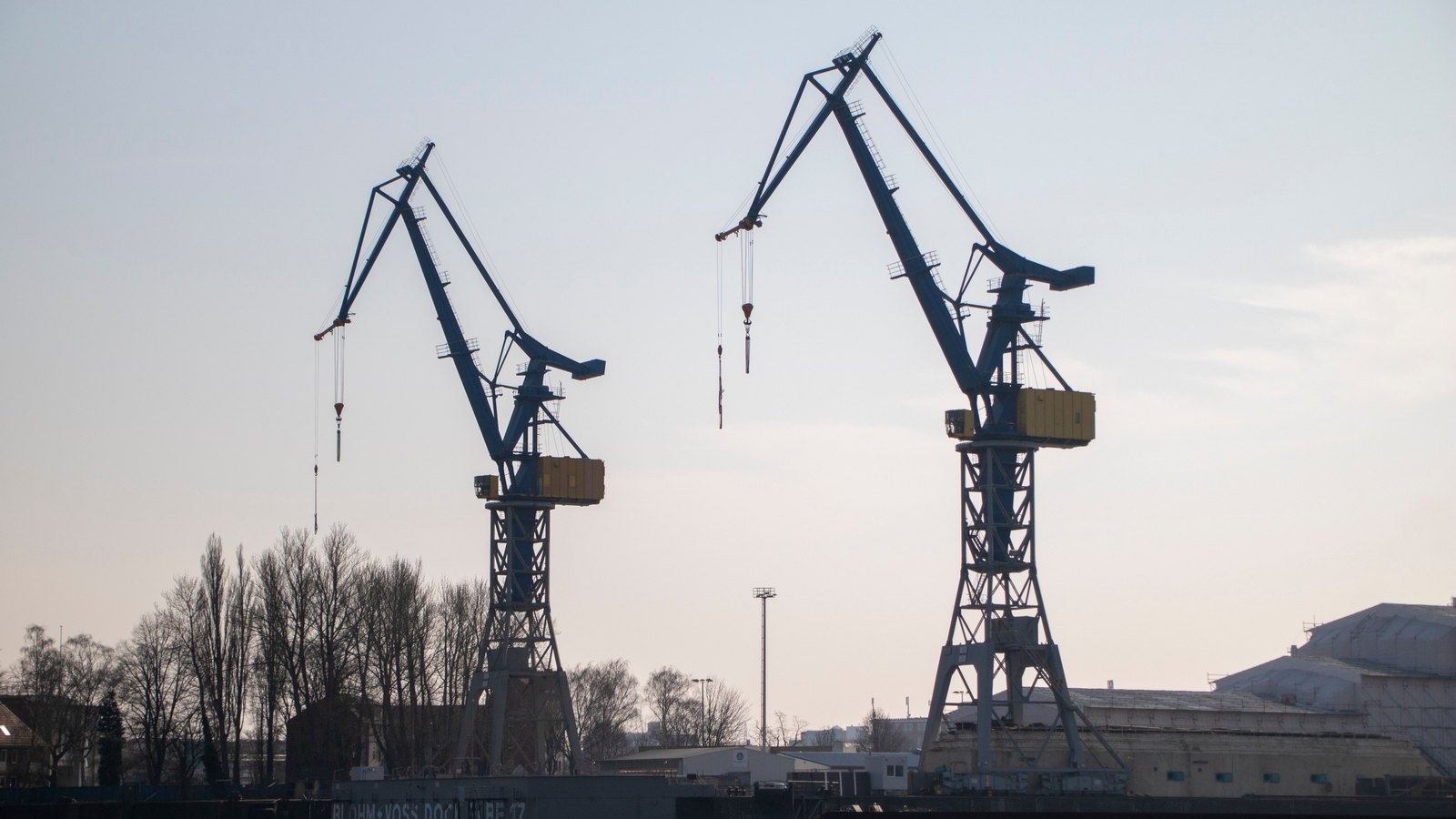 Two cargo cranes silhouetted against a pale sky at a harbor.