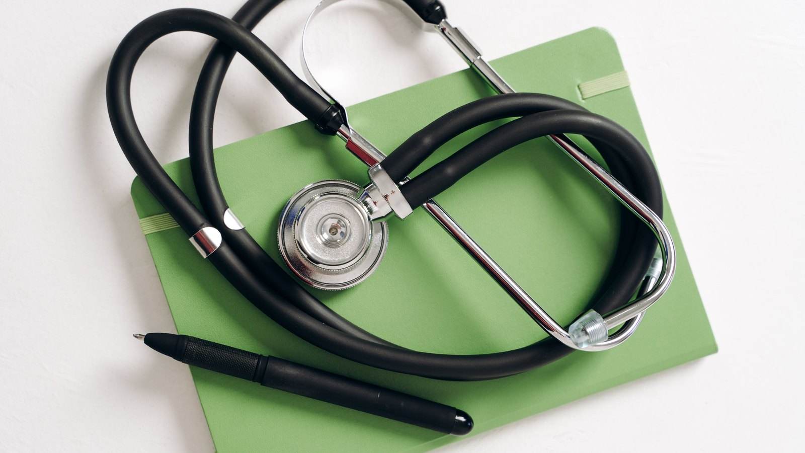 A stethoscope and pen resting on a green notebook.