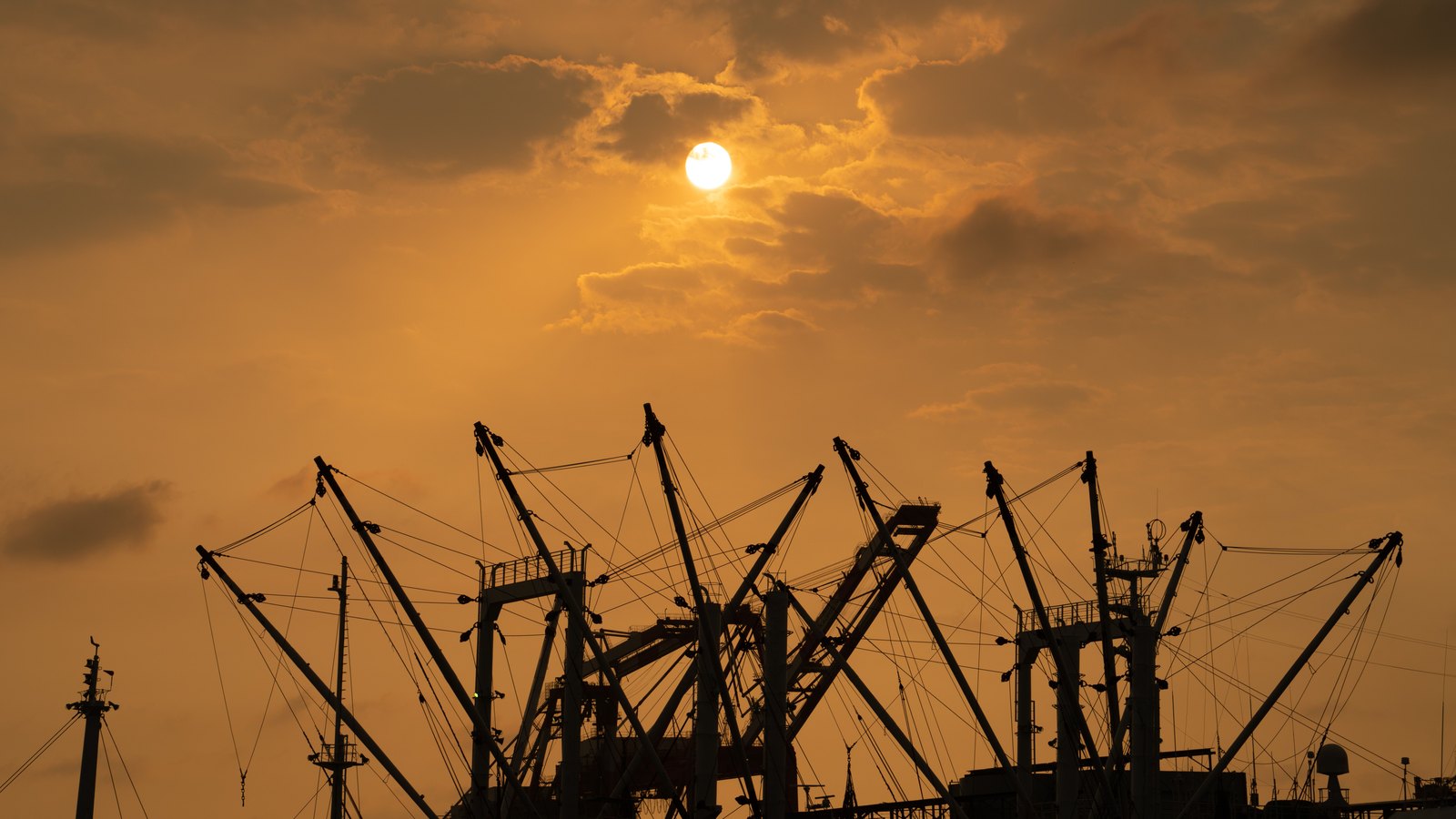 Cargo handling cranes silhouetted against an orange harbor sky.