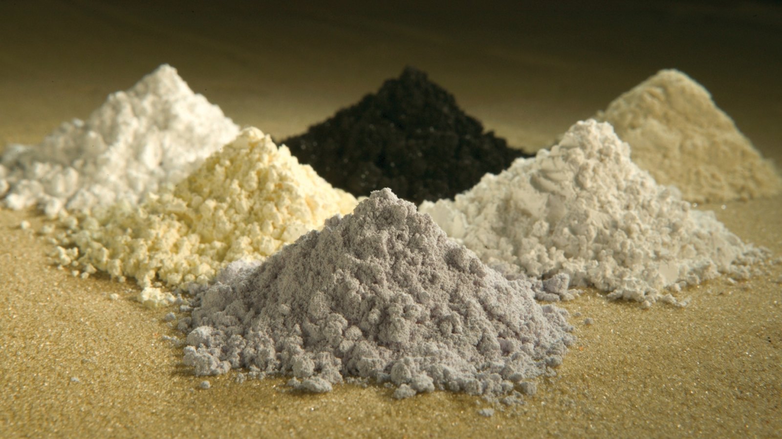 Six mounds of rare earth oxide powders in different colours.