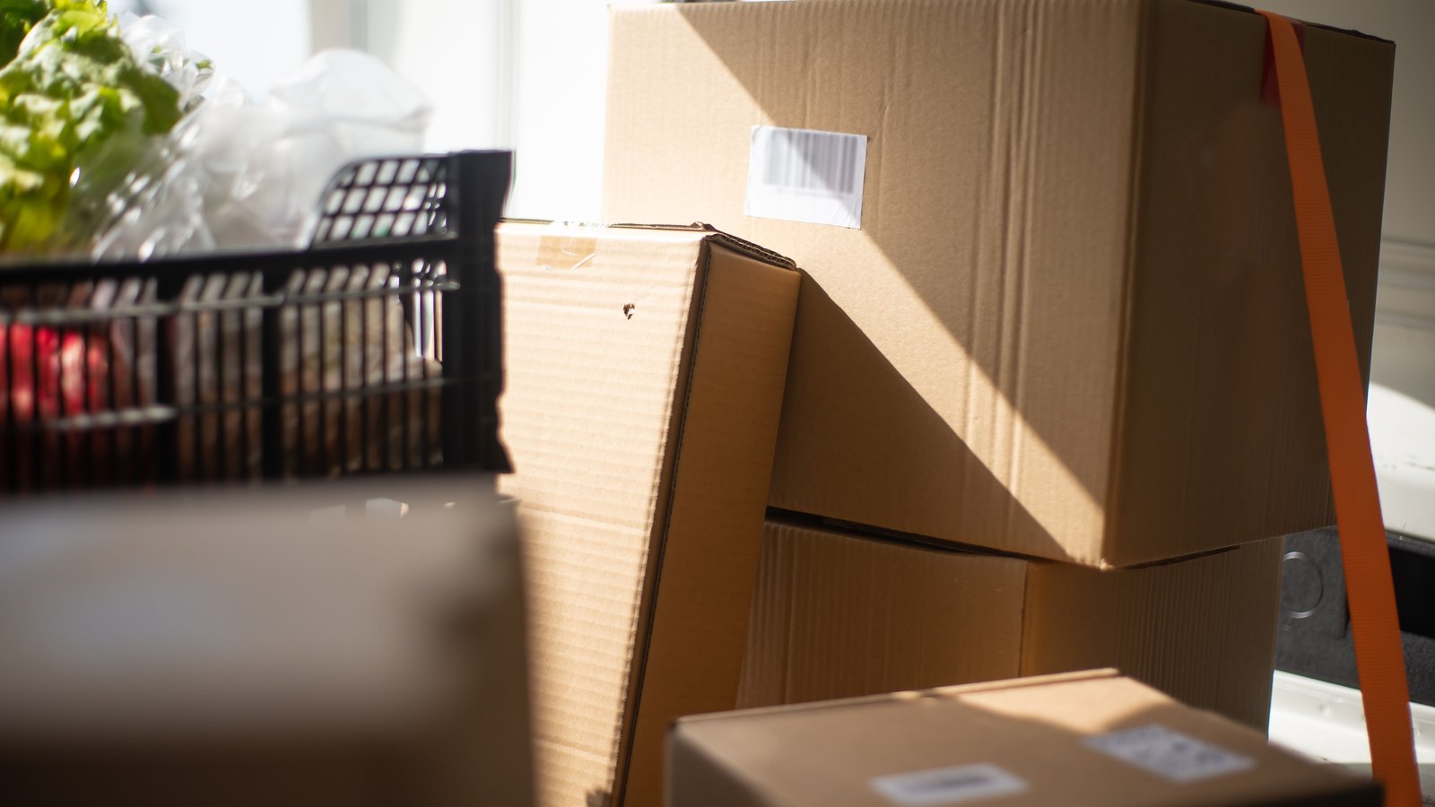 Plain brown cardboard parcels stacked in the back of a van in low sunlight, held by an orange strap, their shipping labels blank at this distance.