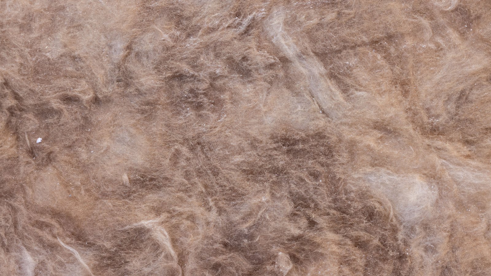 A close photograph of a slab of fibrous mineral wool insulation filling the frame, matted strands of brown and pale tan fibre lying in every direction with no edge, object or text in shot.