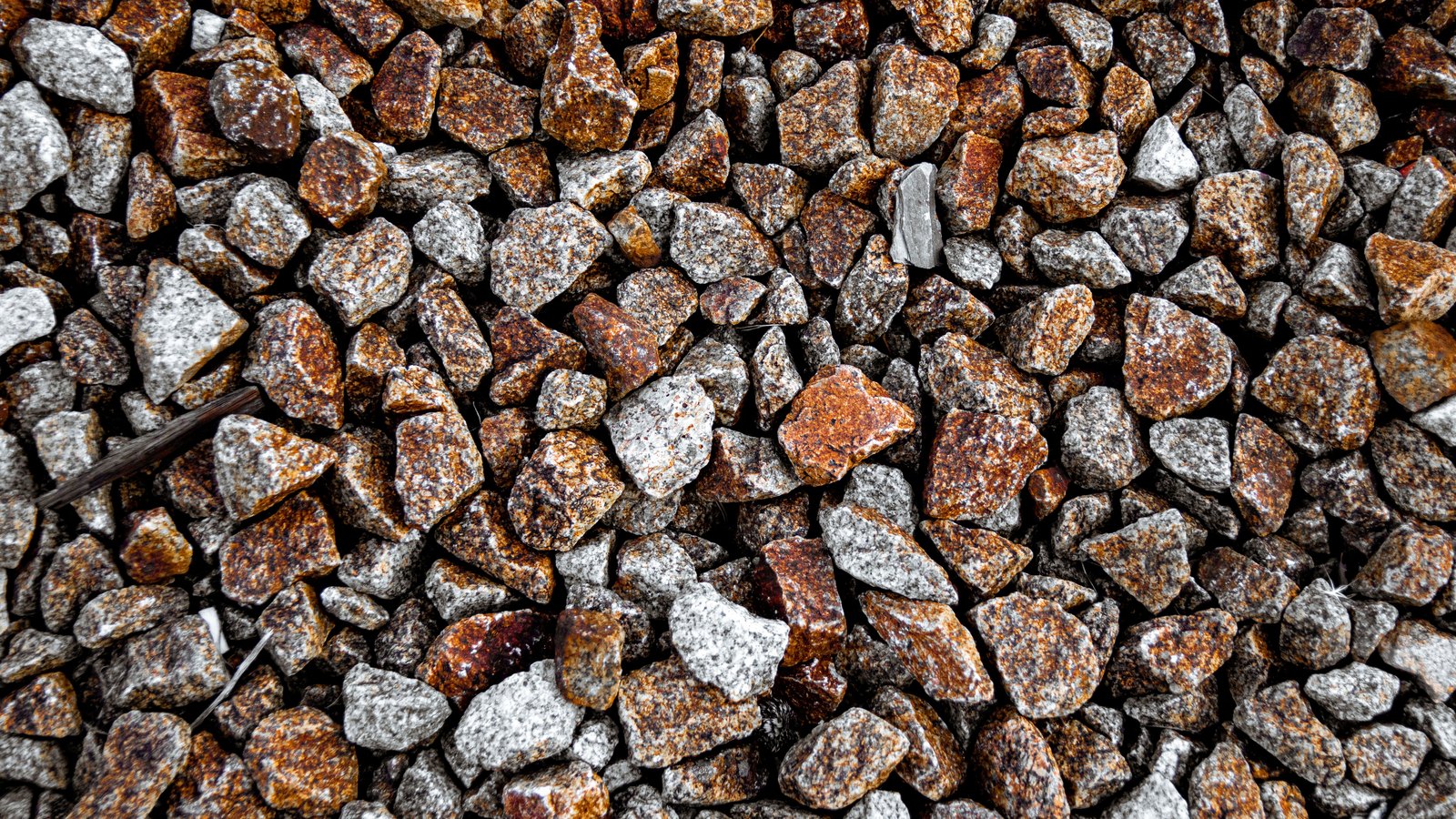 An overhead close-up of crushed stone aggregate filling the frame, angular grey granite and rust-brown chips of roughly equal size.