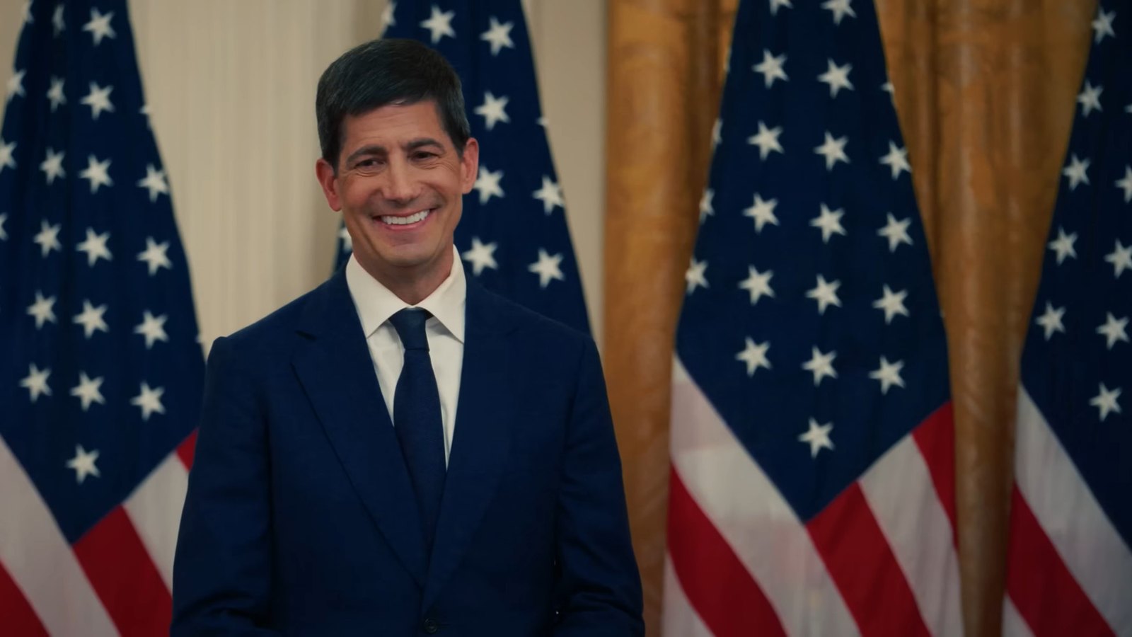 Kevin Warsh in a dark suit and tie, standing before a row of United States flags in a White House room.