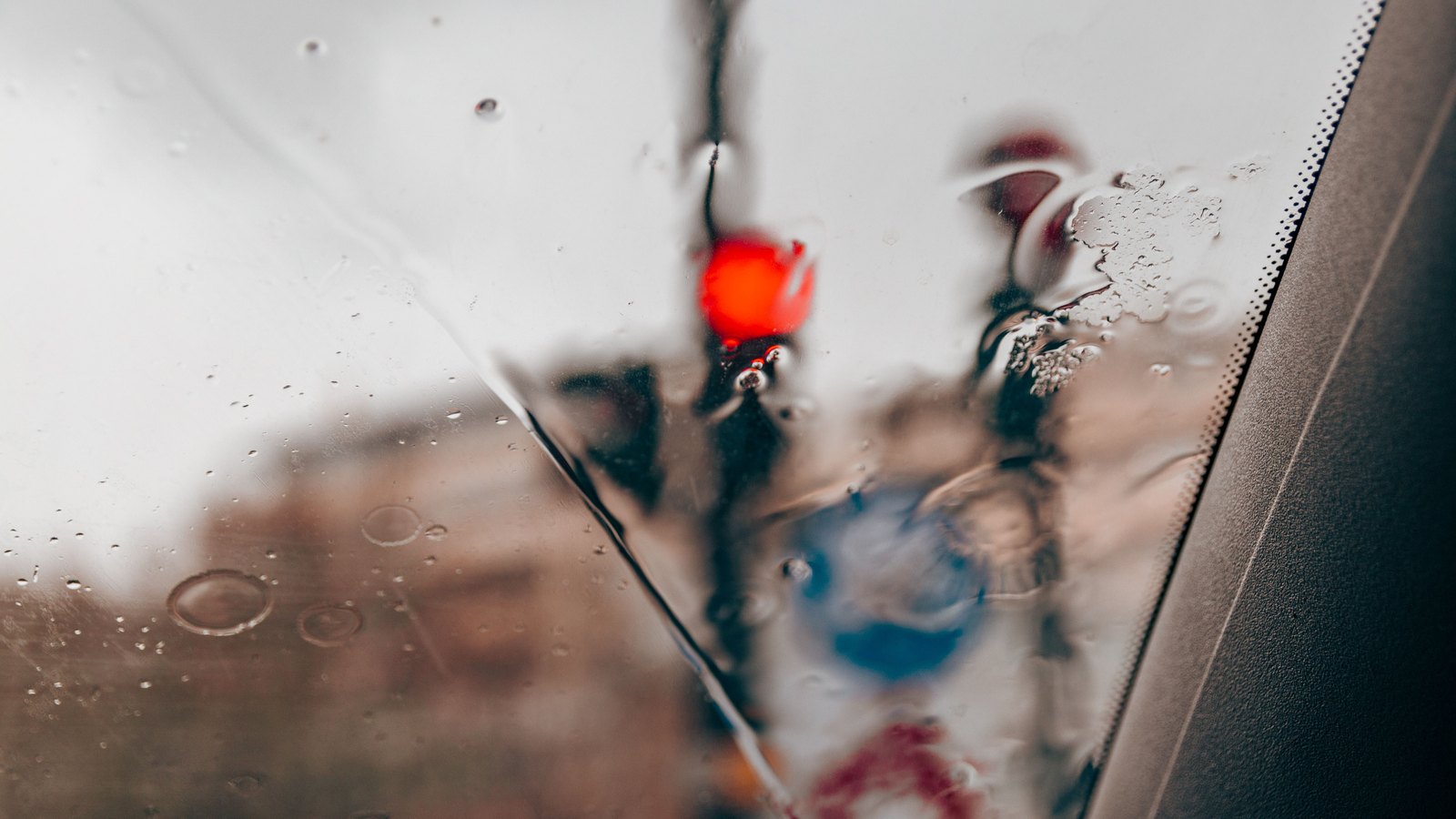 Rain streaks a car window while a cyclist and red traffic light blur beyond it, not a photograph of this advisory.