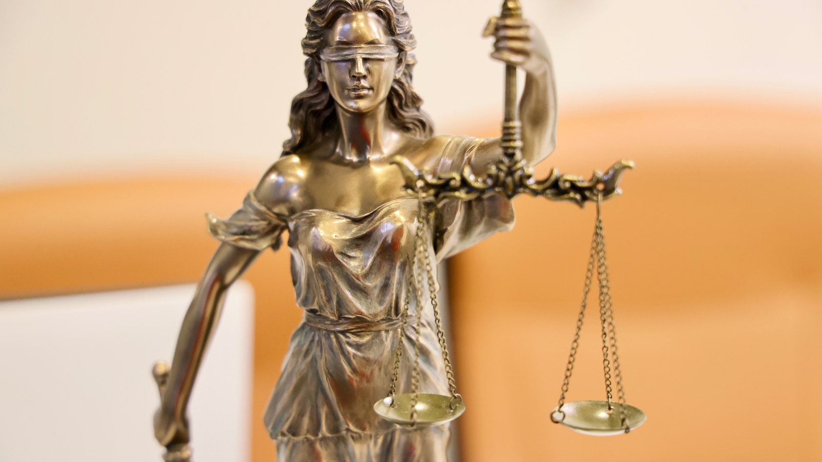 A brass statue of blindfolded Justice on a desk, holding a sword upright in one hand and a pair of empty balance scales level in the other, shot close against a soft out-of-focus interior. No person, no courtroom, no building, no address, no signage, no agency name and no legible text appears in the frame. A stock photograph, not a photograph of this event.