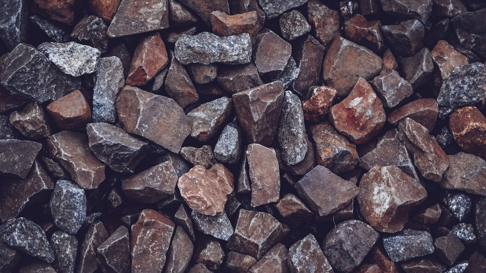 A close view of crushed stone aggregate filling the frame, angular grey and rust-brown pieces packed tightly together.