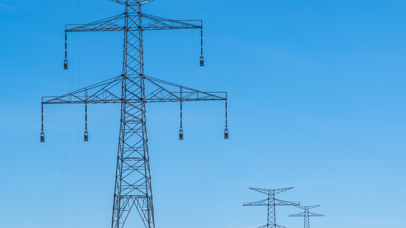 Steel electricity transmission towers against a clear blue sky.