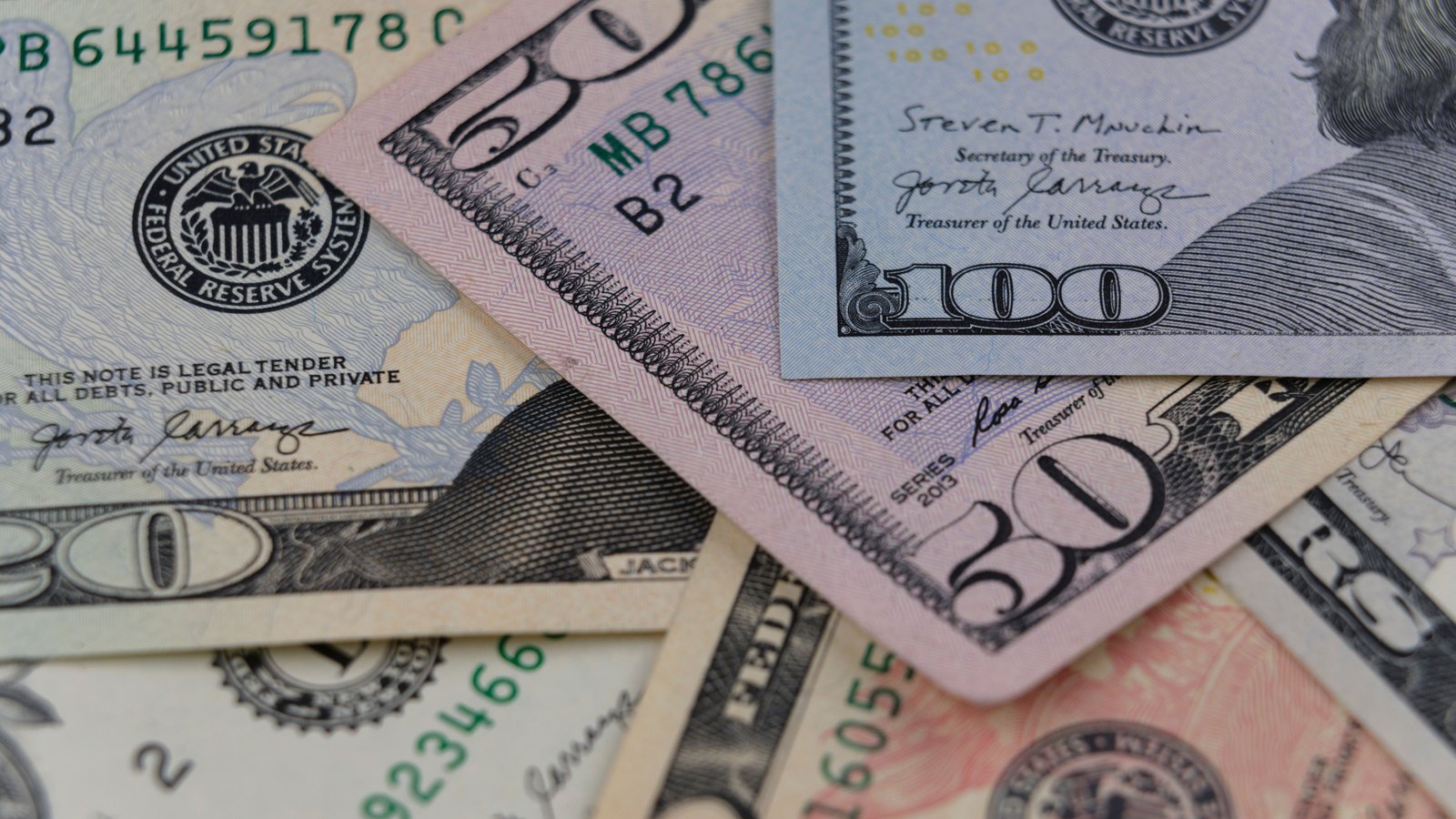 A close overlapping arrangement of United States one hundred dollar and fifty dollar bills on a flat surface.