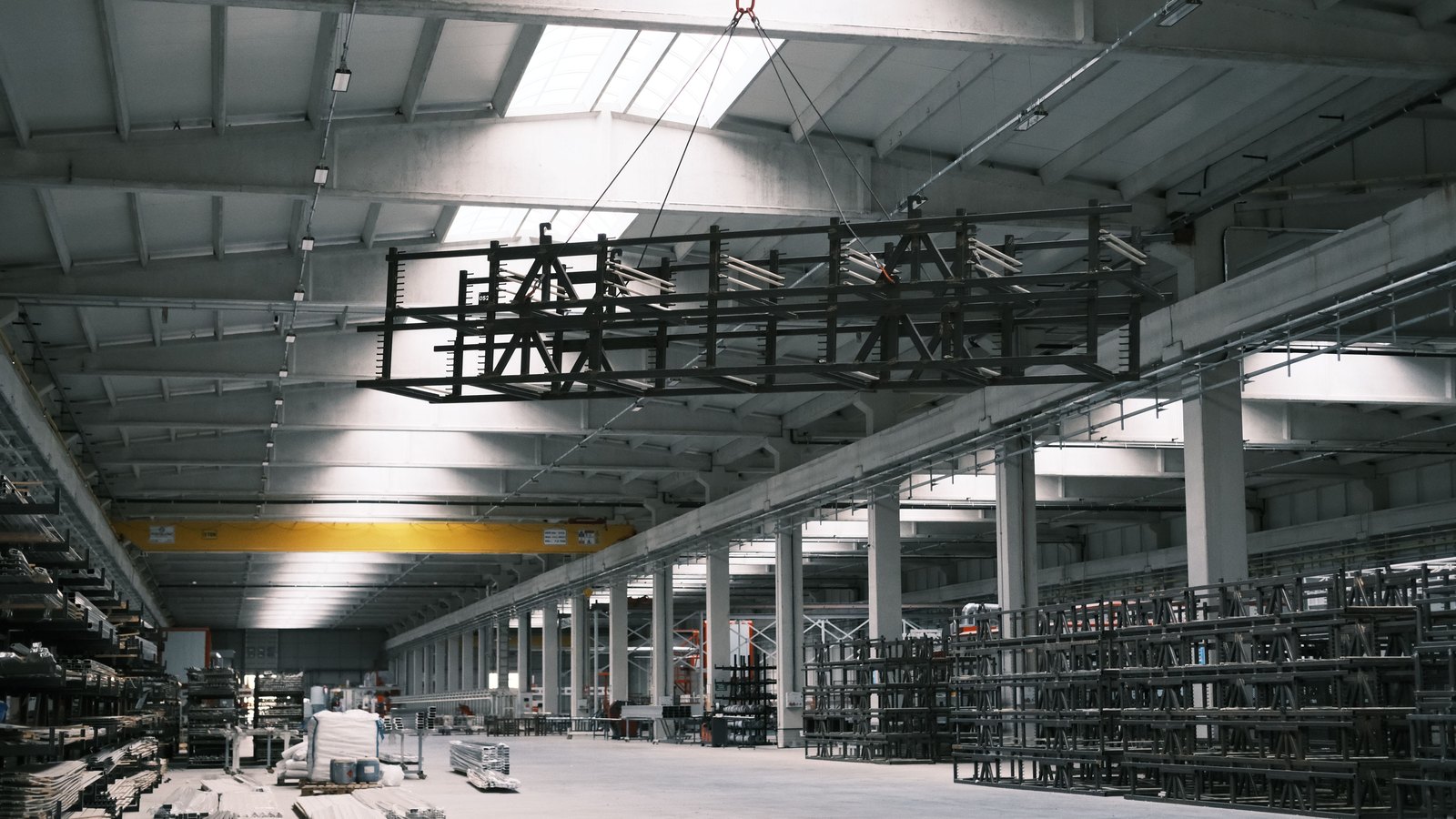A wide industrial hall with an overhead crane and rows of steel racking.