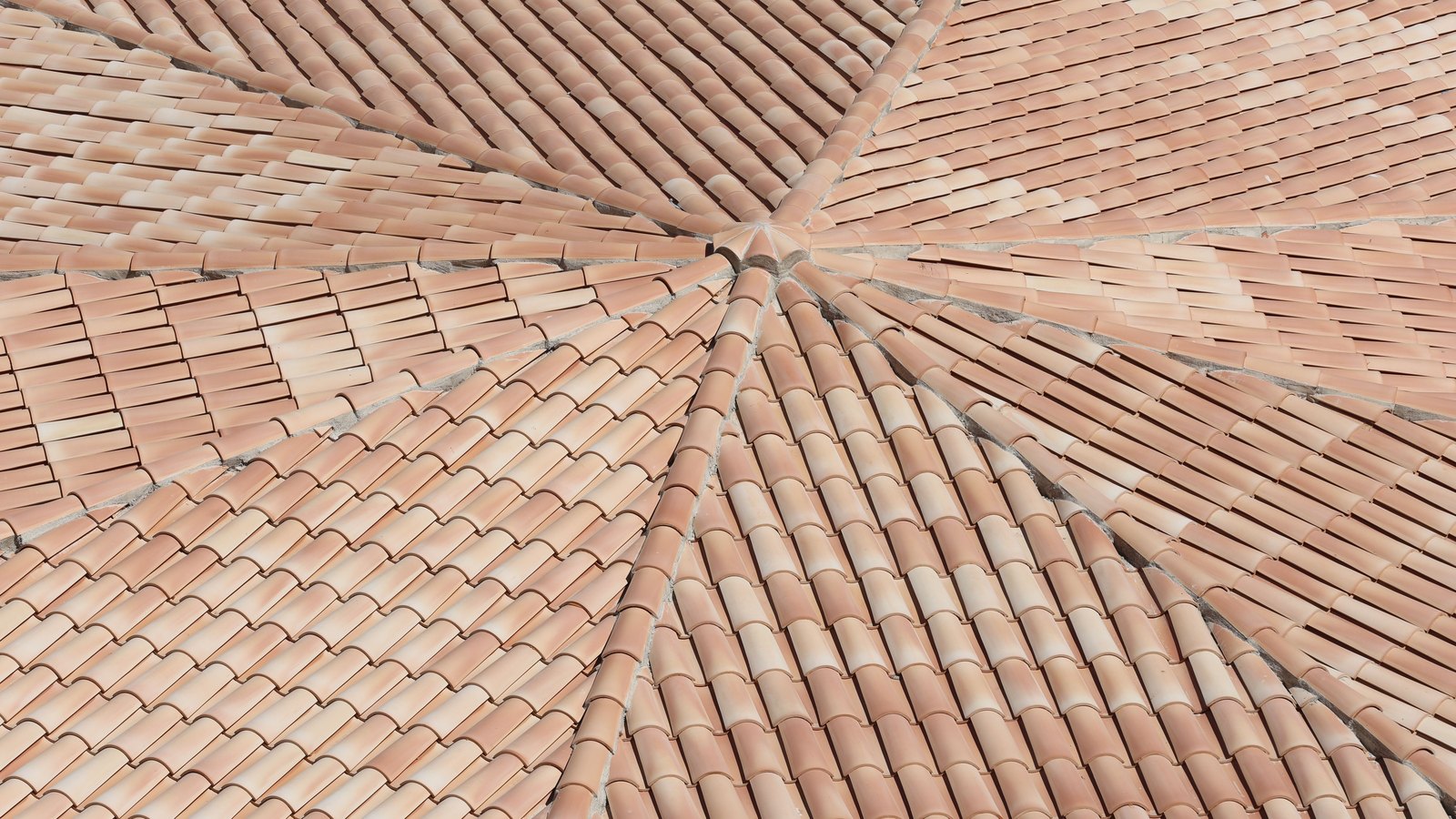 Barrel roof tiles seen from above, the rows fanning out from a single point where several roof planes meet.
