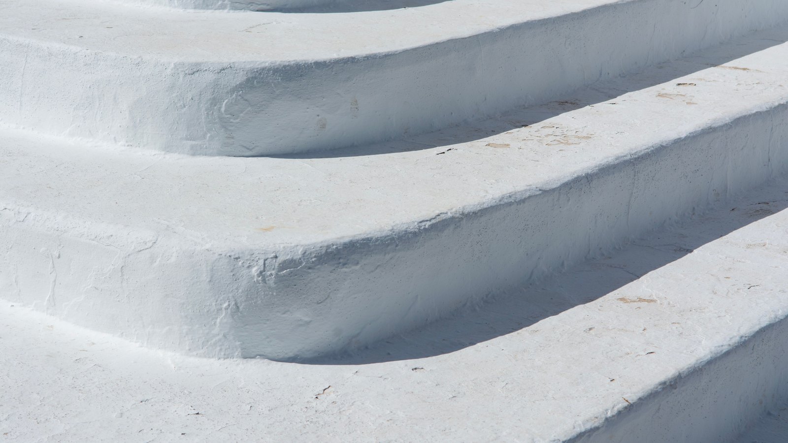 Four white painted stone steps in bright sunlight, seen close up from the side.