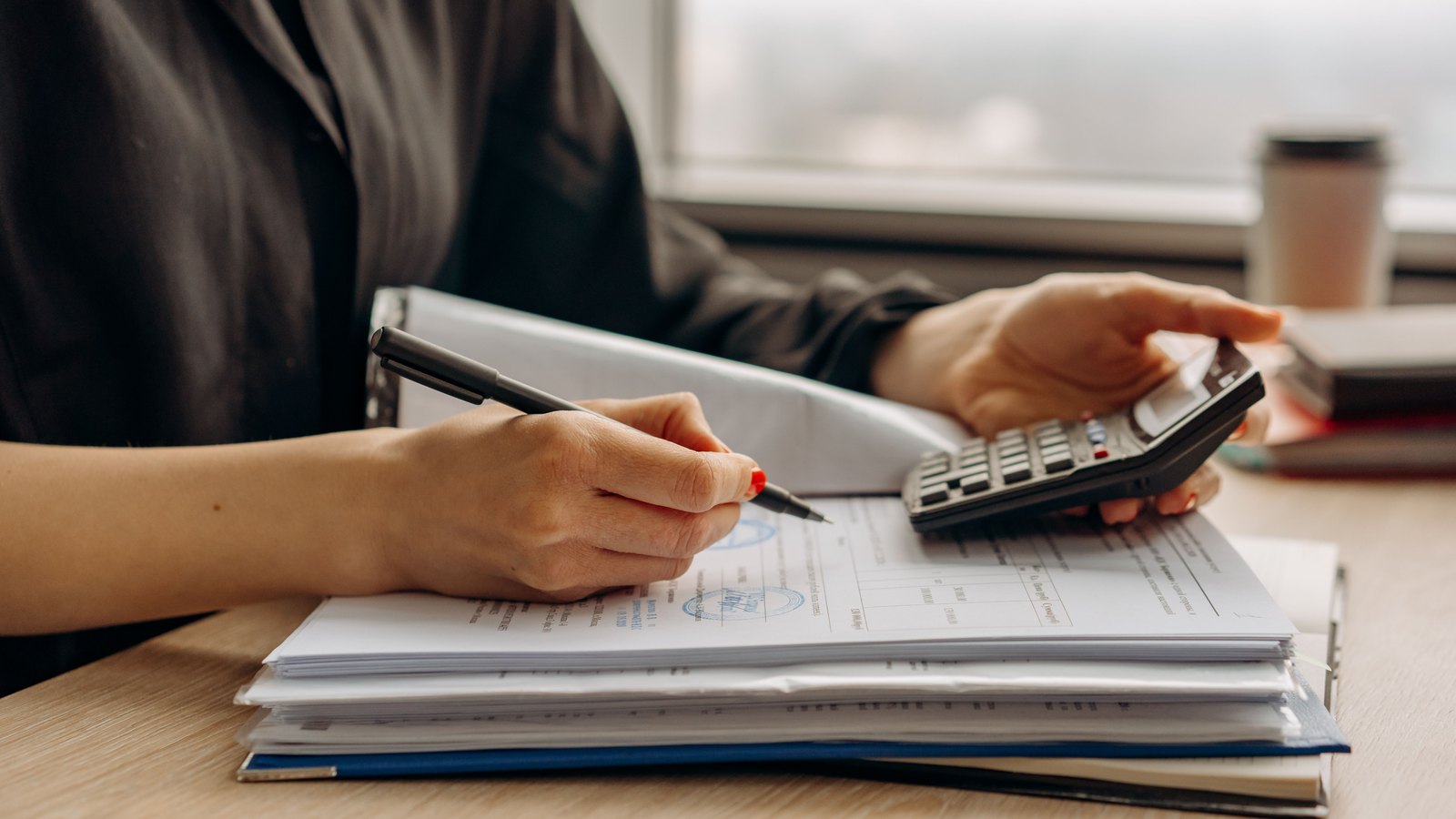 Hands use a calculator over financial papers at an office desk