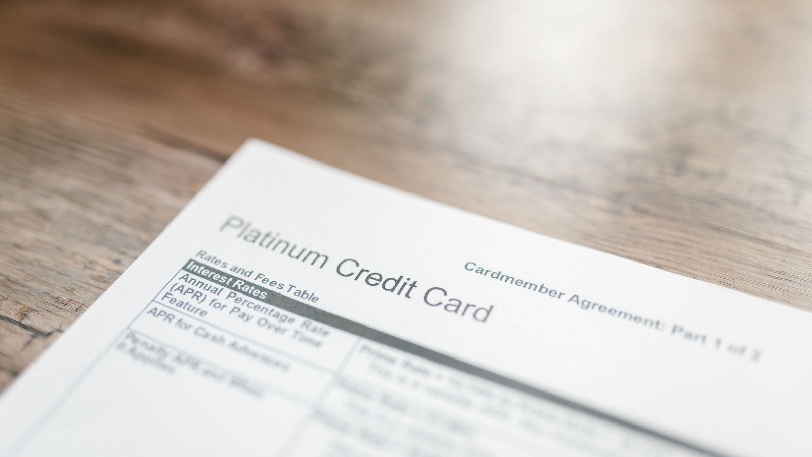 A credit card agreement on a wooden table, open at the rates and fees table, with most of the type falling out of focus.