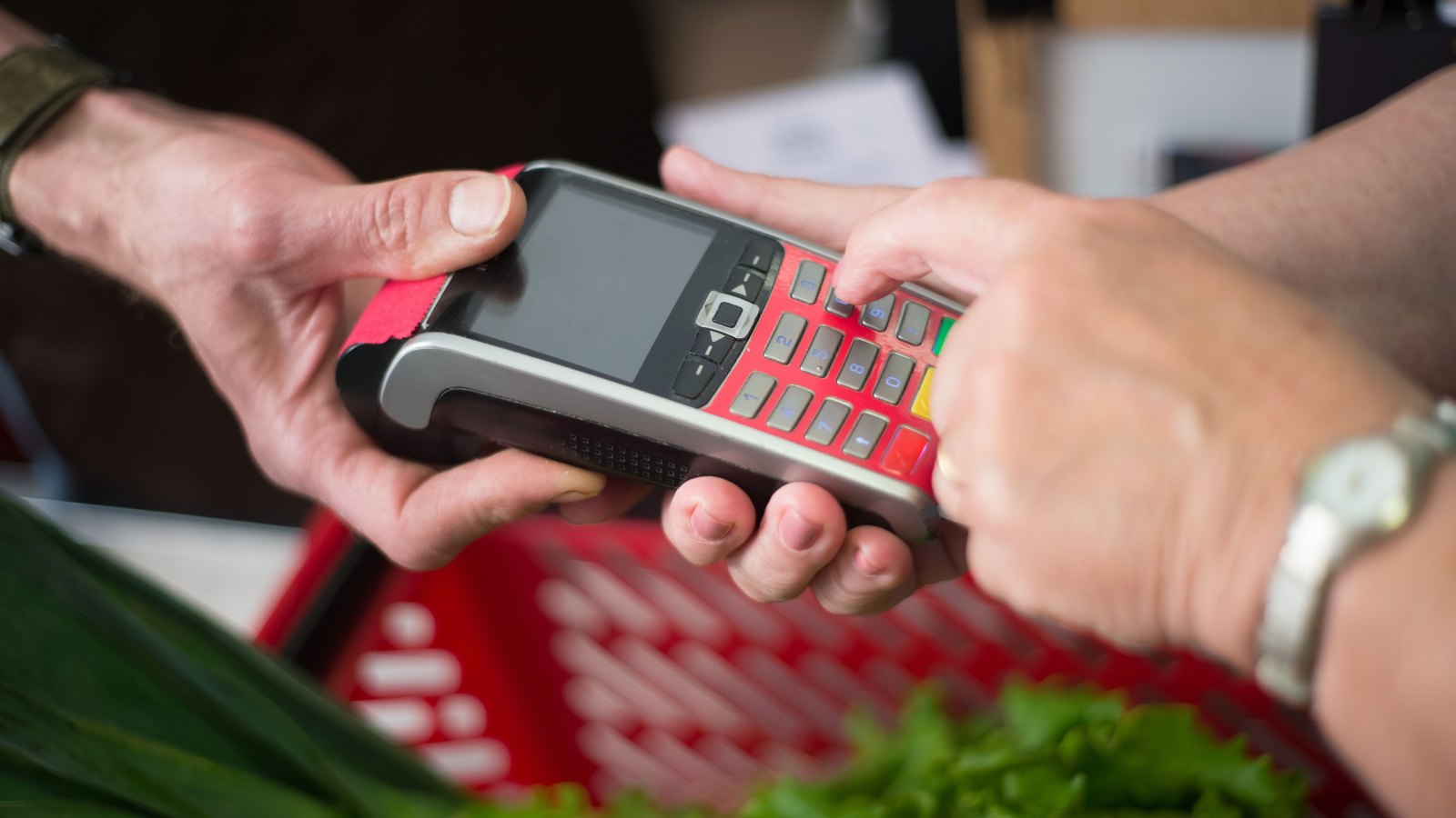 Two pairs of hands holding a card payment terminal at a shop checkout, its screen blank