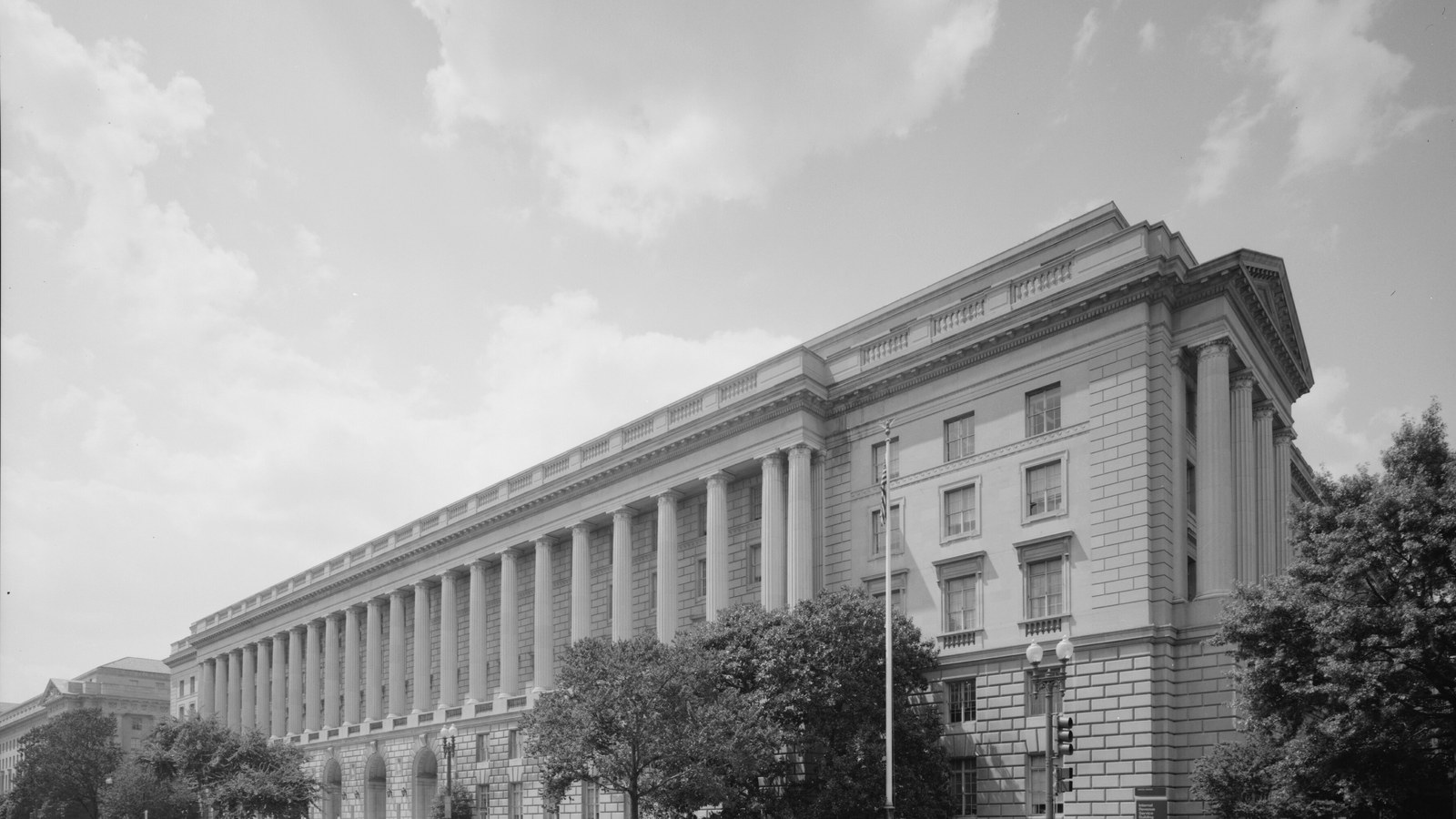 A black and white architectural survey photograph of the Internal Revenue Service headquarters at 1111 Constitution Avenue in Washington, showing the long Ionic colonnade running the length of the Constitution Avenue facade and the pedimented corner pavilion.