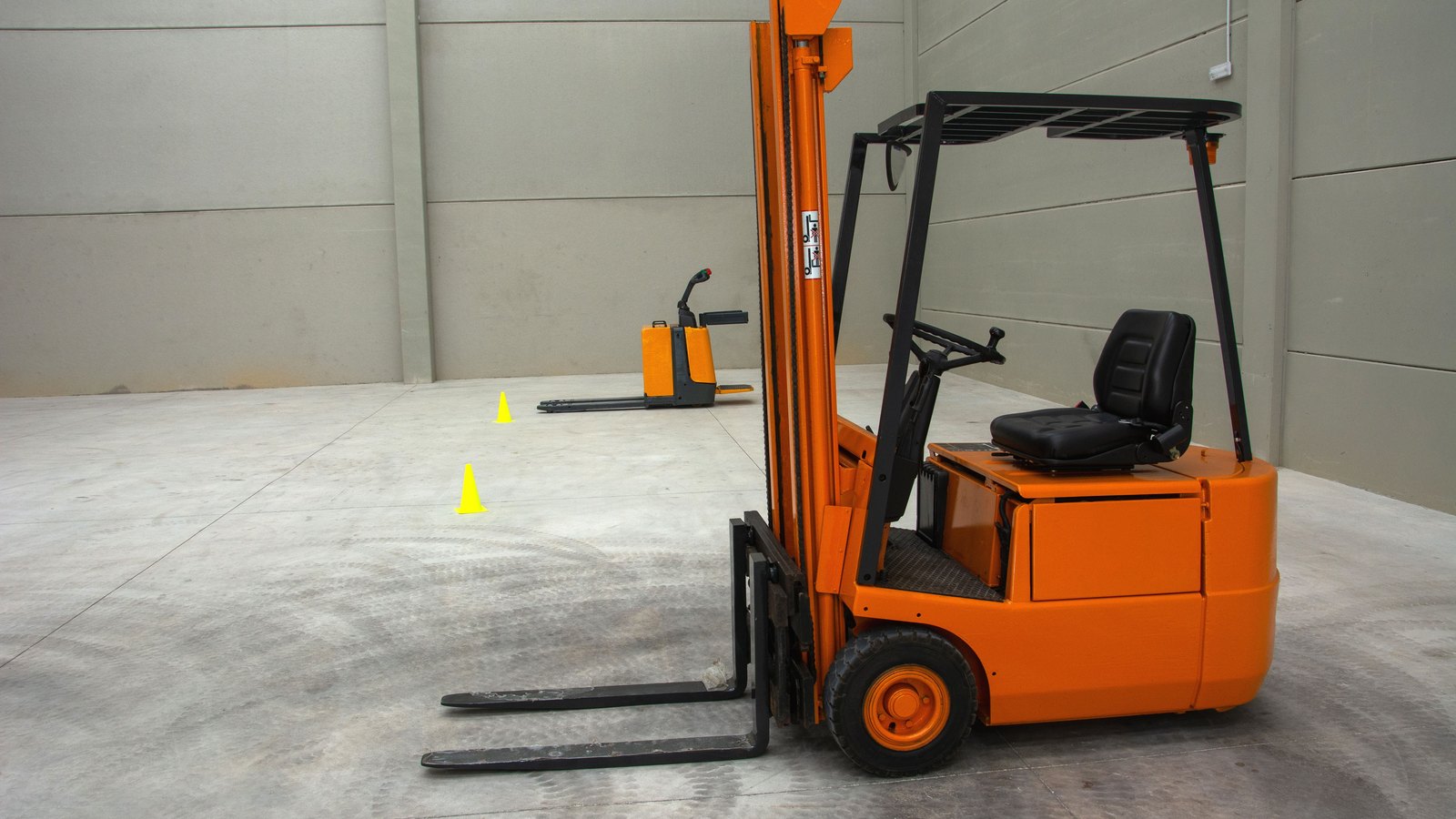 An orange forklift parked on a concrete floor in an empty warehouse.