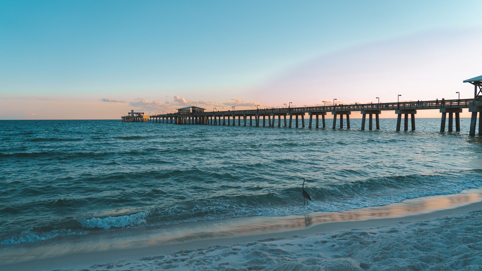 A fishing pier over the Gulf of Mexico at sunset on a white-sand Florida beach.