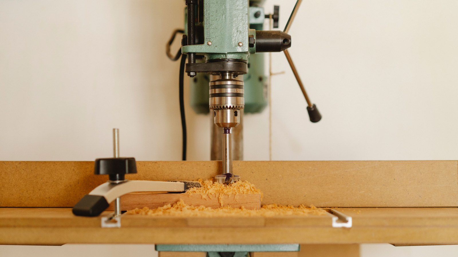 A drill press cutting into a wooden board in a workshop