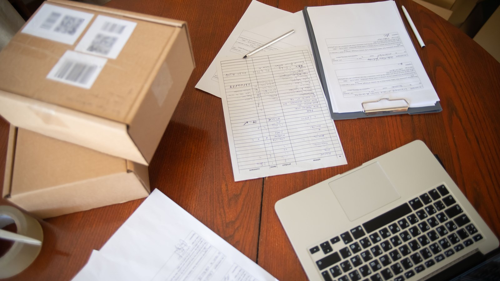 An itemised form and a signed document on a table beside packed cardboard boxes and a laptop