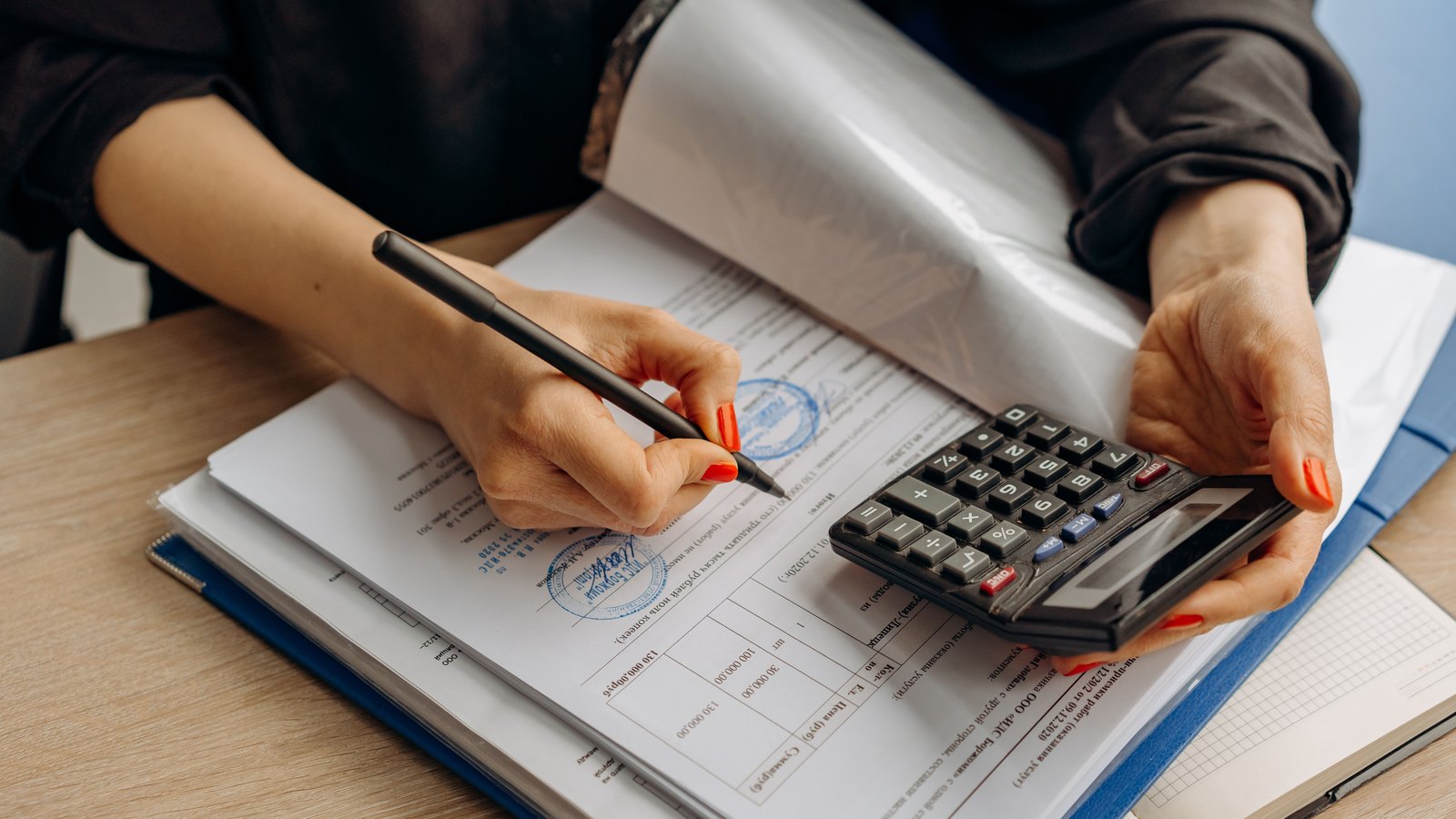 Hands turning pages of a stack of stamped financial paperwork while holding a calculator