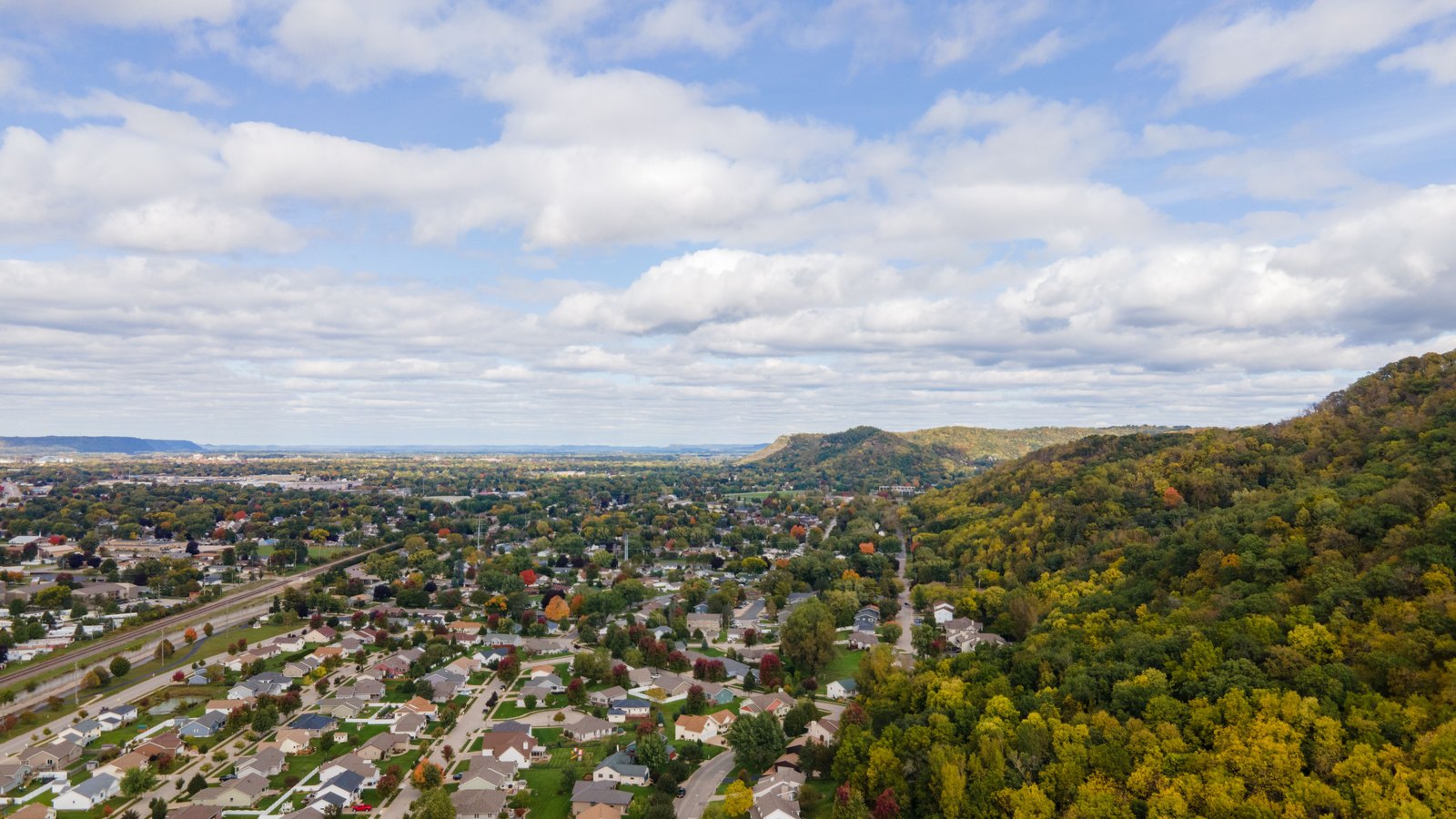 An aerial view of an American residential neighborhood beside a wooded hillside.