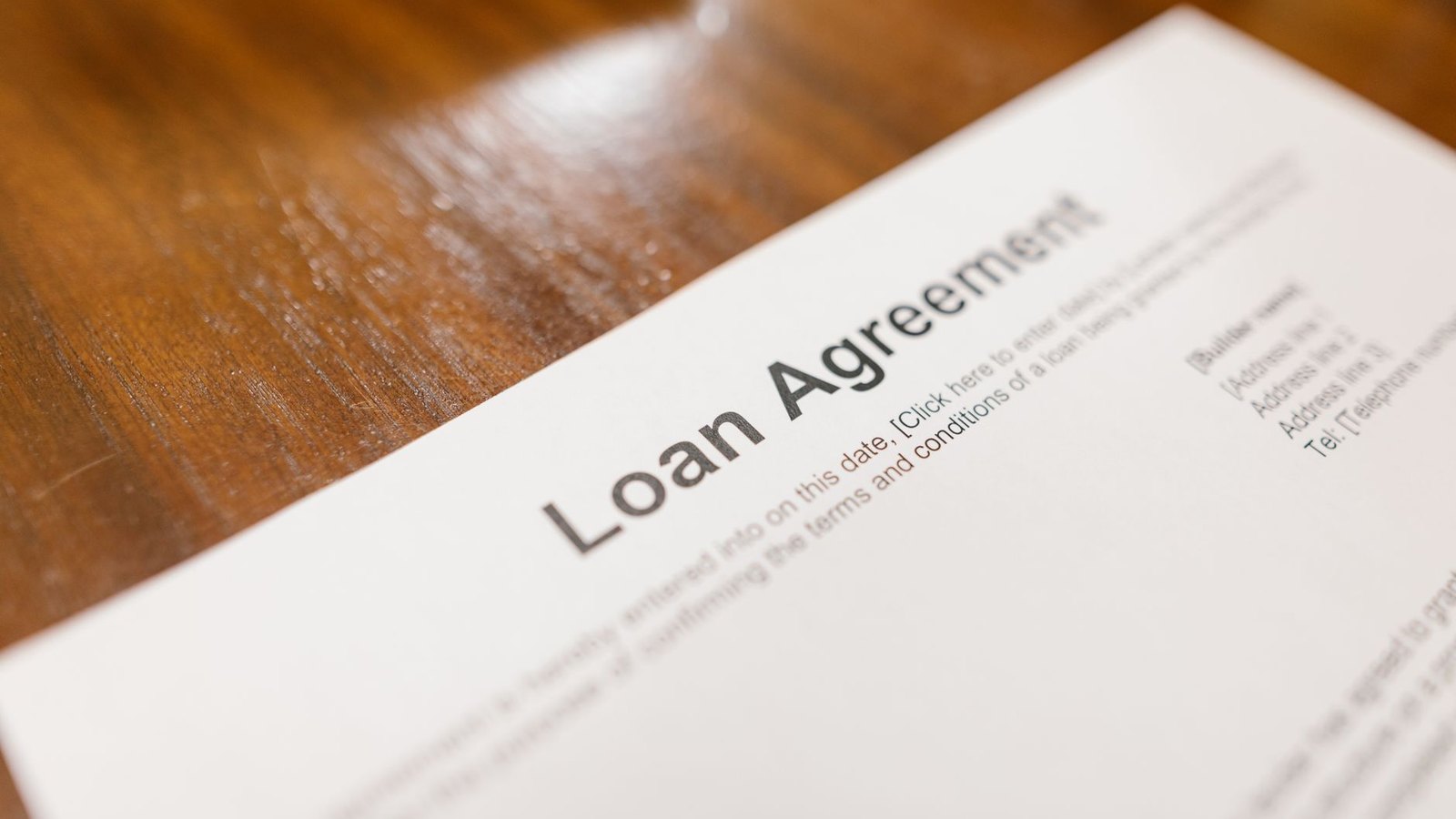 A printed loan agreement lying at an angle on a scratched wooden table, its heading and template placeholder text visible.