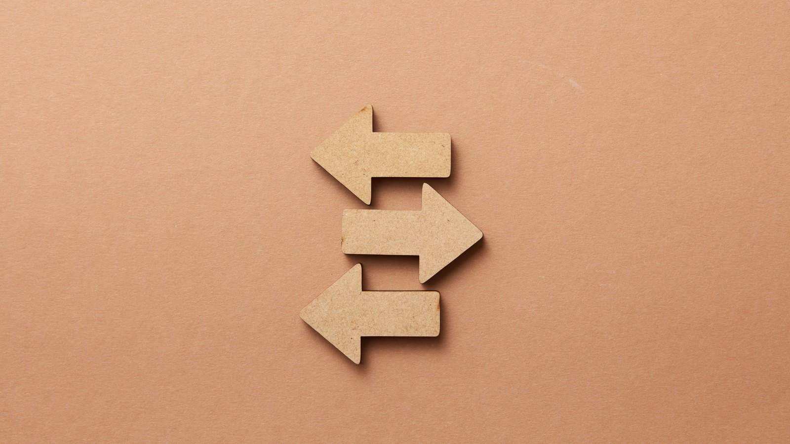Three flat wooden arrow shapes on a plain tan background, two pointing left and one pointing right.