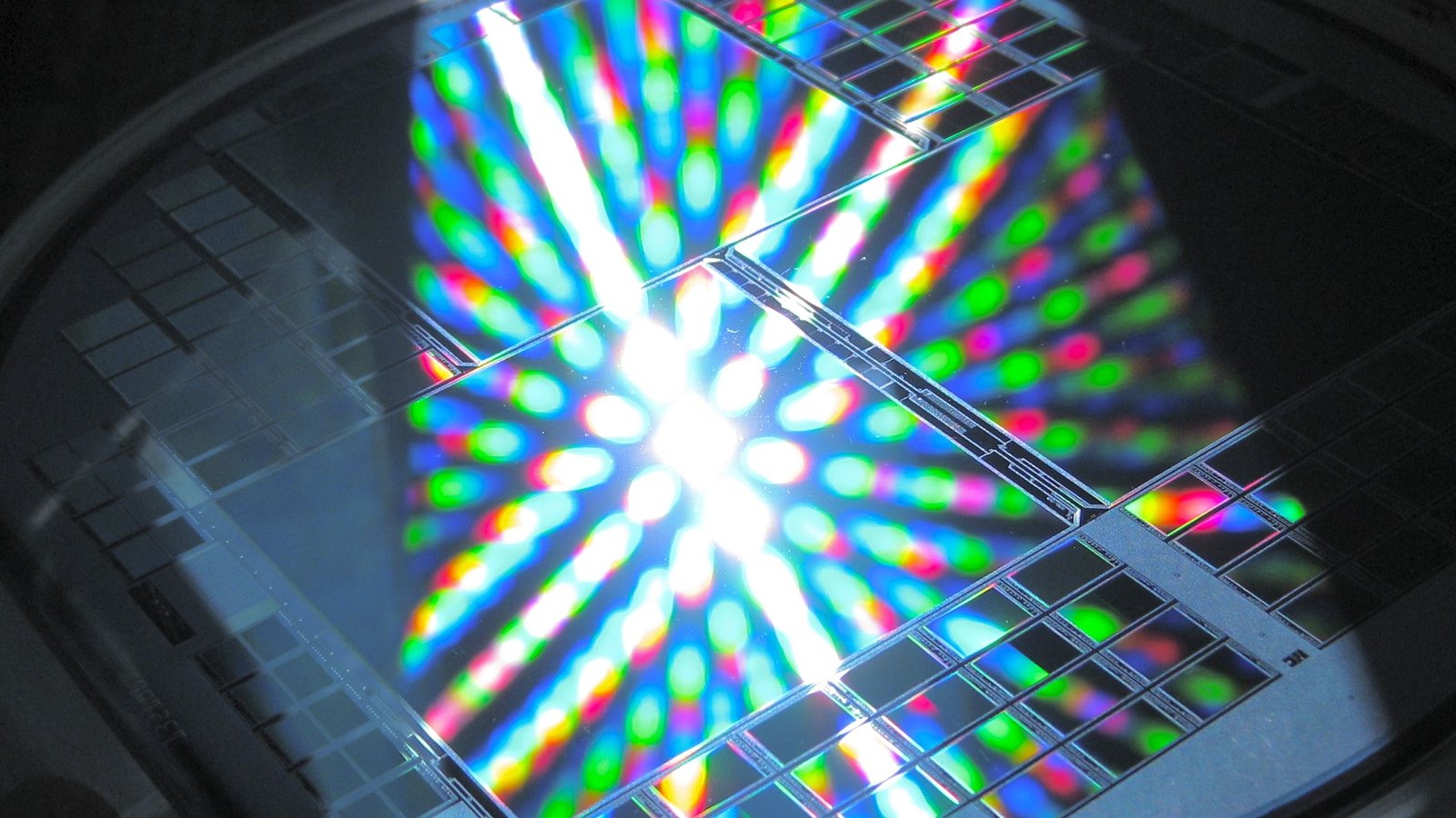 Colored light reflects across the patterned dies of a semiconductor wafer.