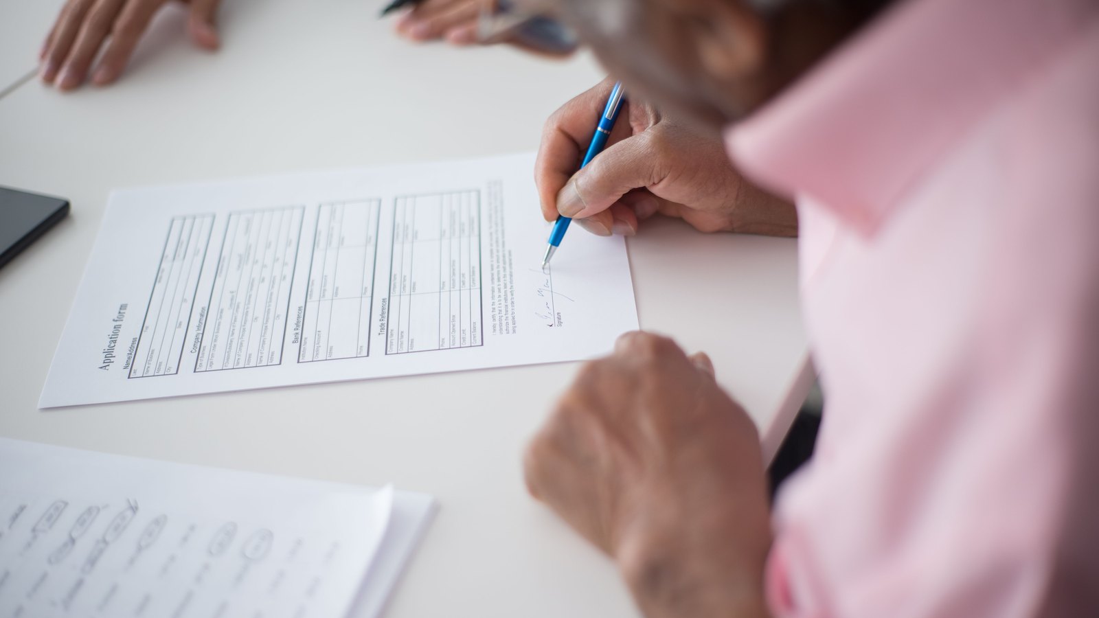 An older homeowner signs an application form at a desk