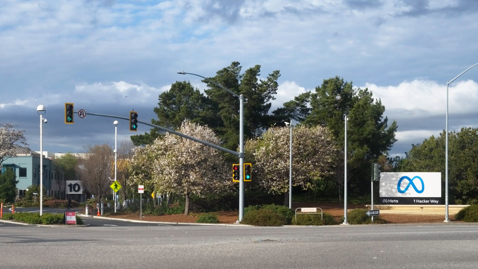 The entrance to Meta Platforms' headquarters campus in Menlo Park, California, with a sign reading 1 Hacker Way beside a road intersection, photographed in March 2022.